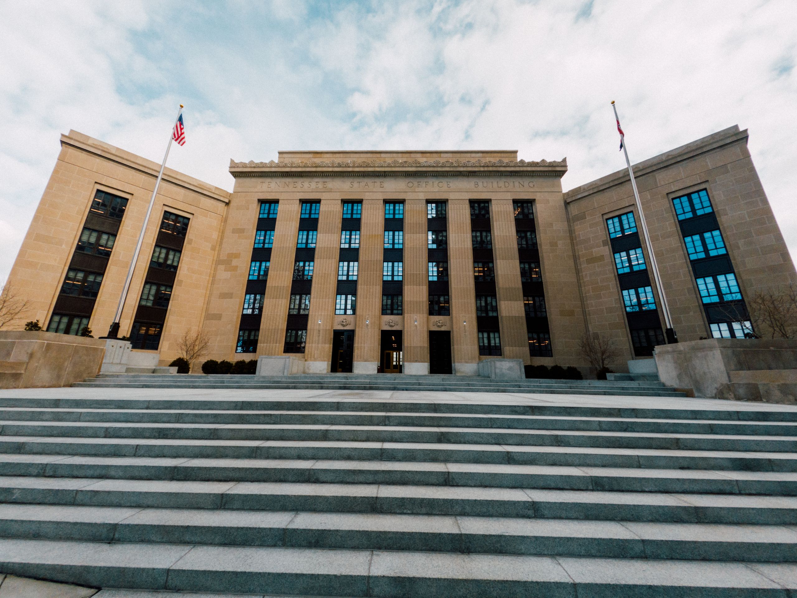 From below of Federal Reserve building exterior against USA flags and staircase under cloudy sky in town