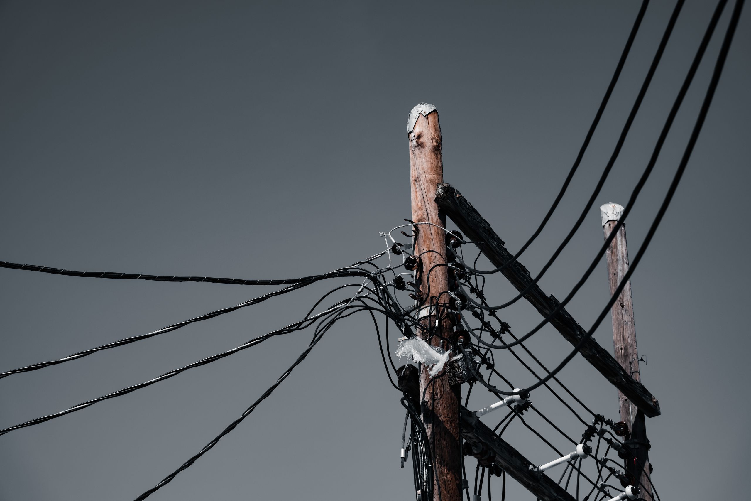 Low angle shot of wooden utility poles with power lines against a gray sky in Orlando, FL.