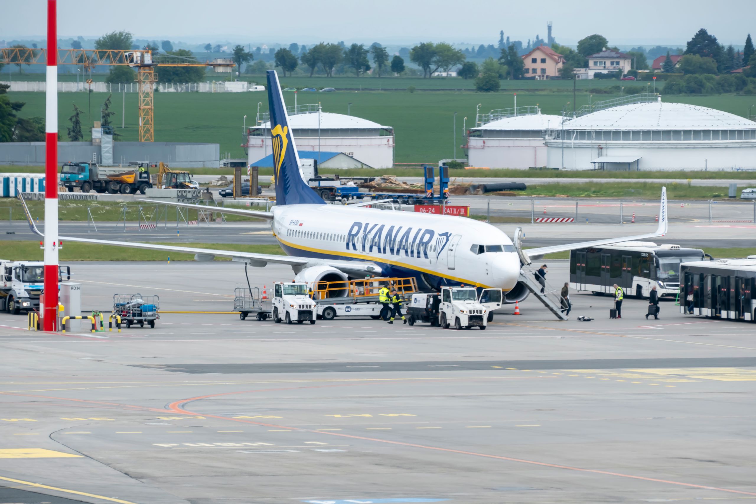 Passengers and crew prepare a Ryanair plane for departure at a bustling airport terminal.