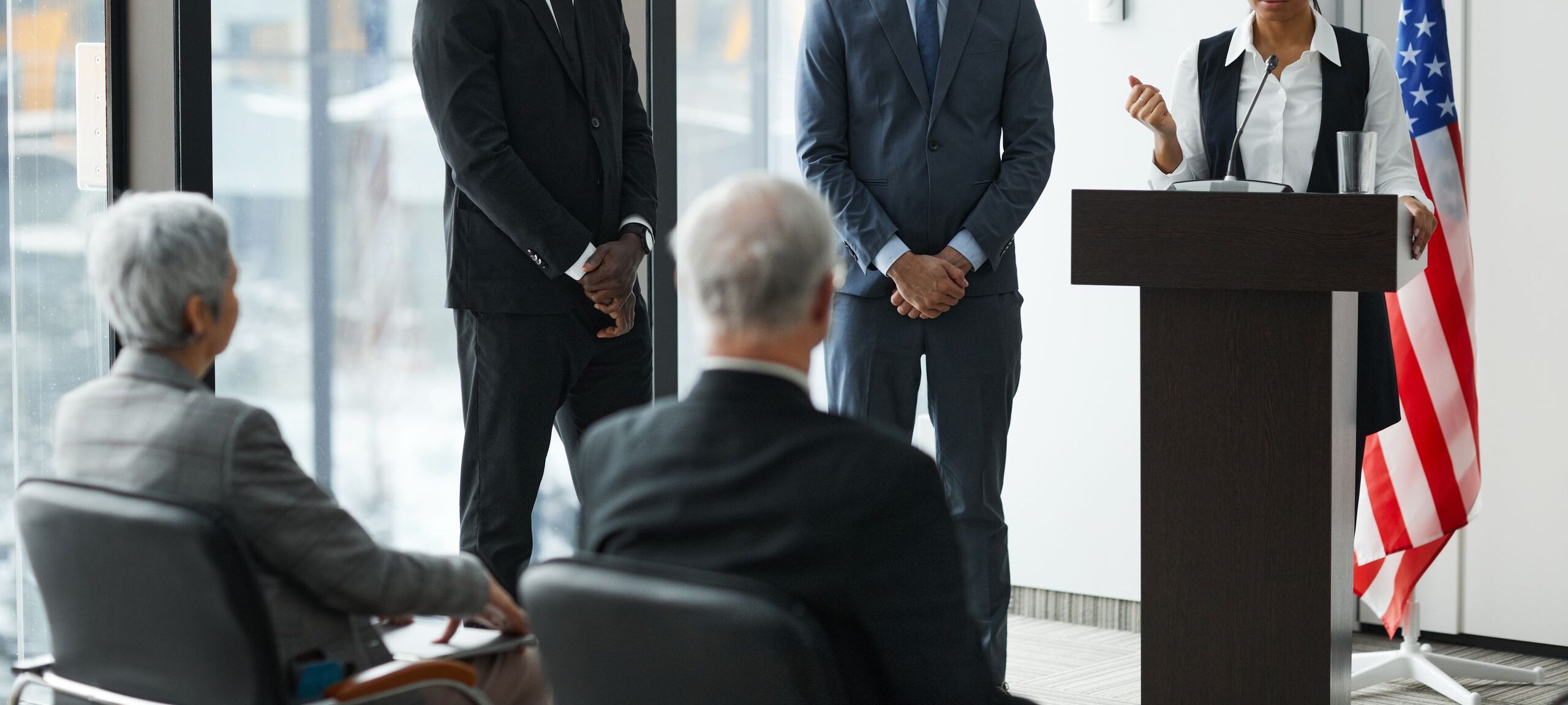 Professional speakers presenting at a conference in a modern room with glass windows.