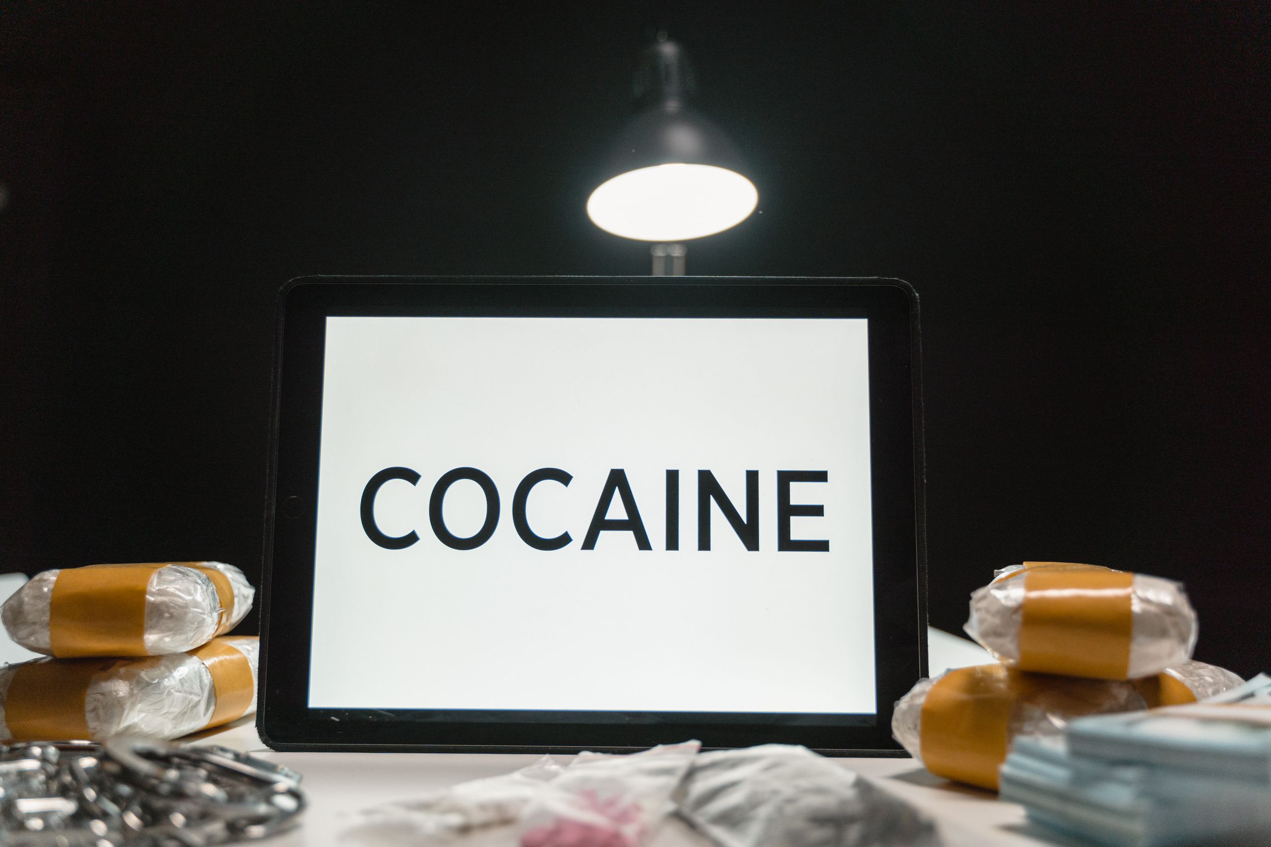 Tablet computer displaying the word 'Cocaine' surrounded by wrapped packets in a dimly lit setting.