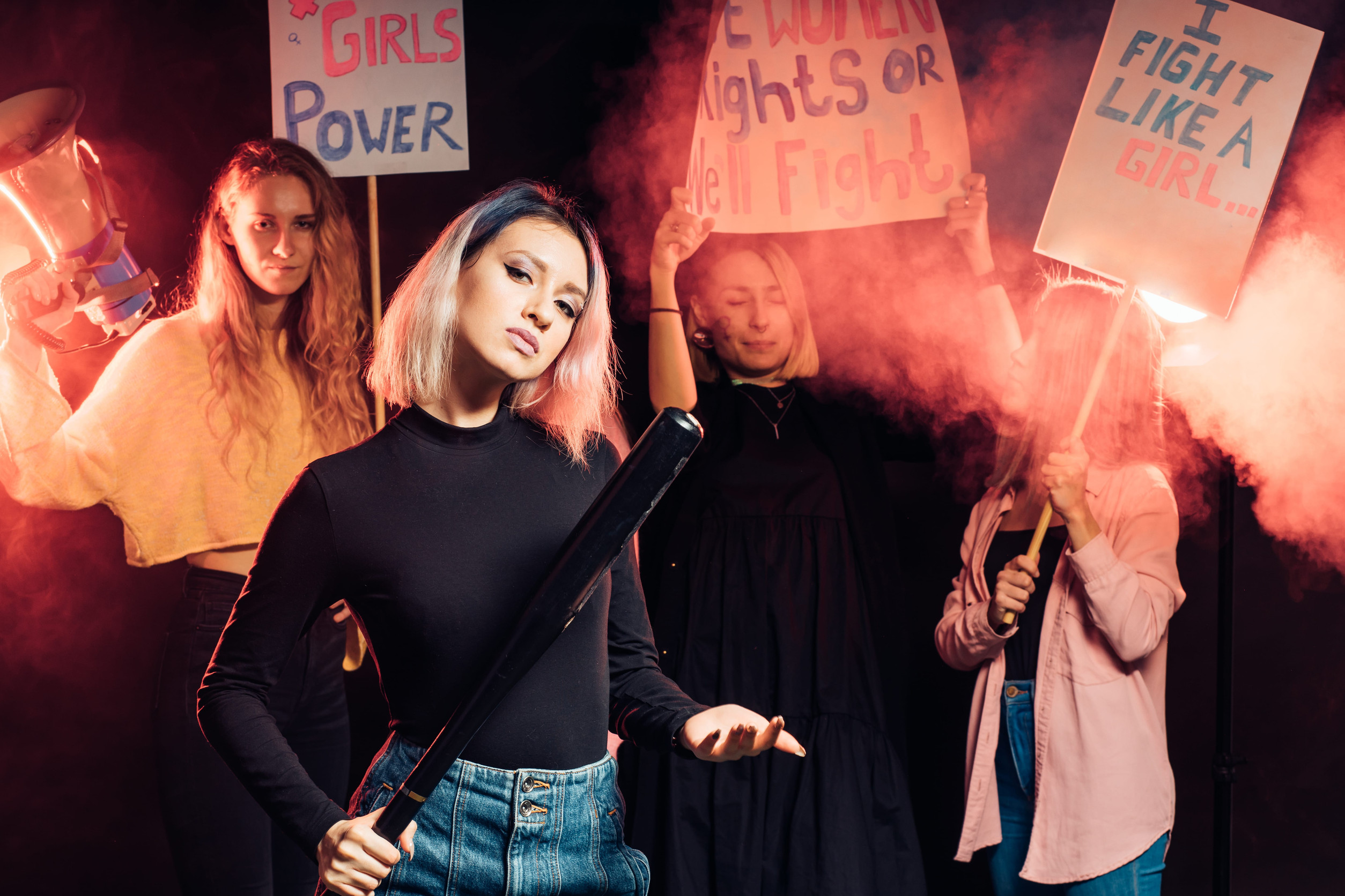 young caucasian female feminist stand holding bat isolated in smoky space, fight for woman rights promoting feminists movement