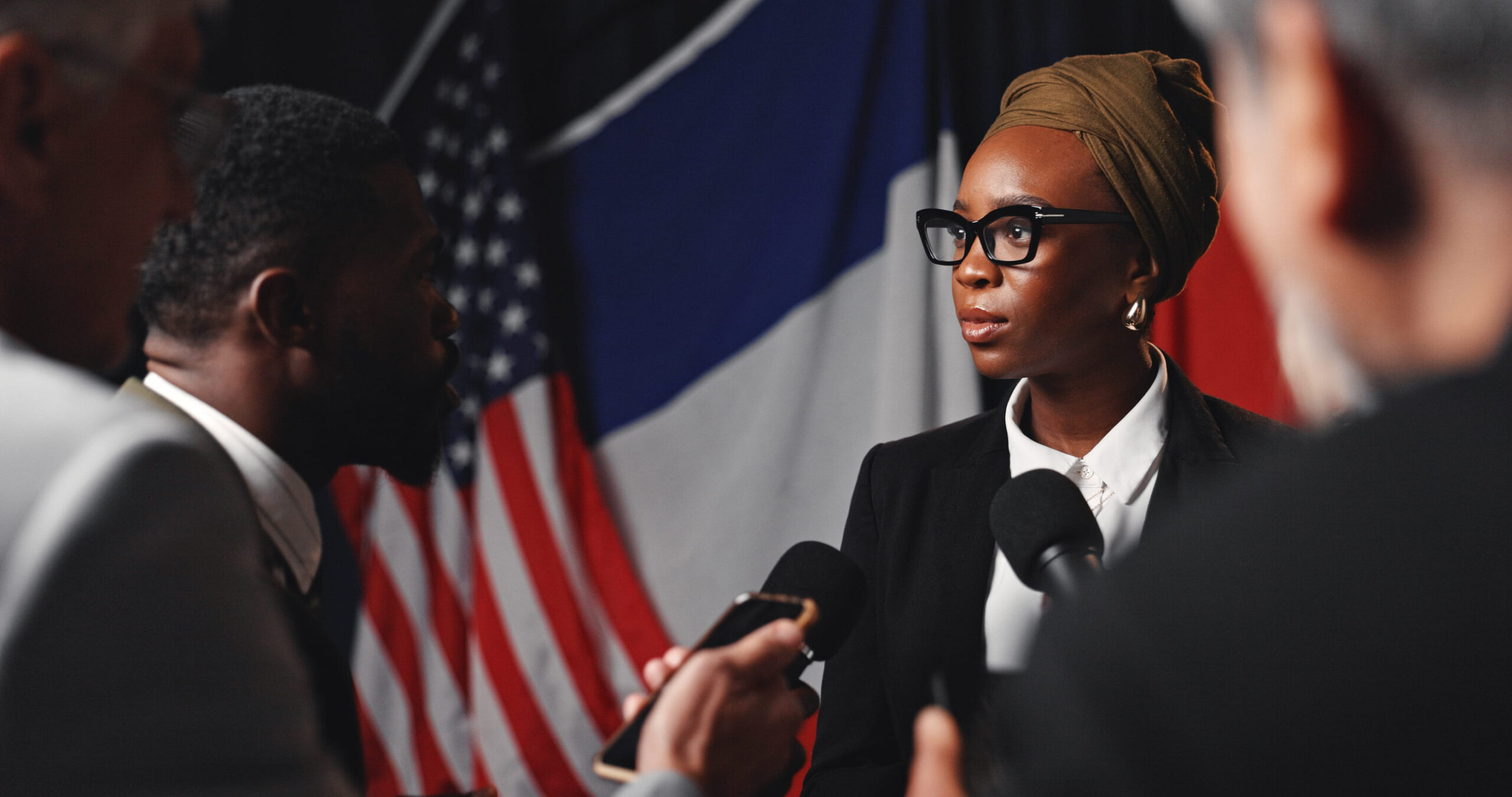 Woman, press conference and flags at international convention, journalist group or interview at event. Person, speaker or ambassador with media, mic and talk for peace negotiation to stop global war