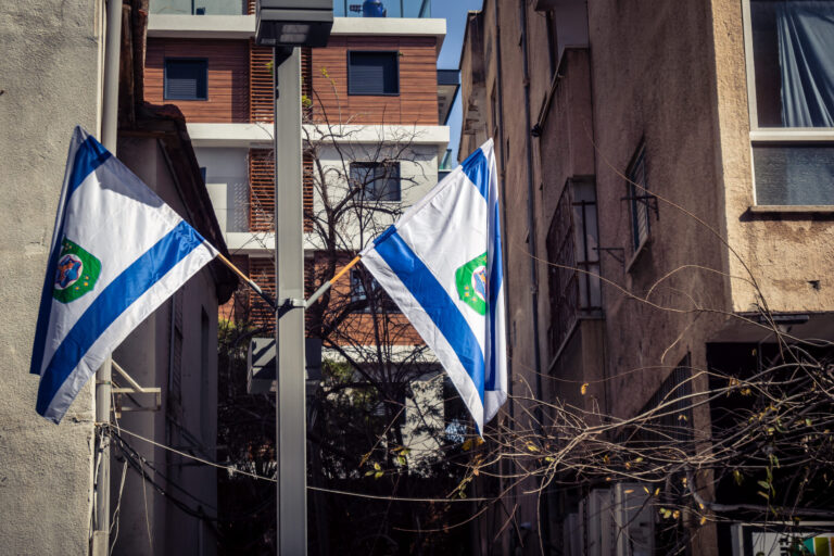 Tel Aviv, Israel, March 12, 2026 The national flag of Israel with the Star of David and the municipal flag of Tel Aviv-Yafo fly side by side in a public street. These symbols represent national pride and local identity in the Israeli metropolis.