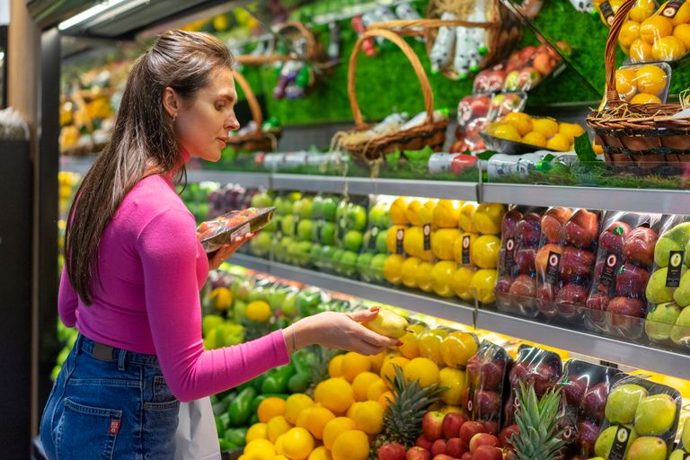 A woman examines fresh fruits in a vibrant grocery store produce section, shopping for healthy options.