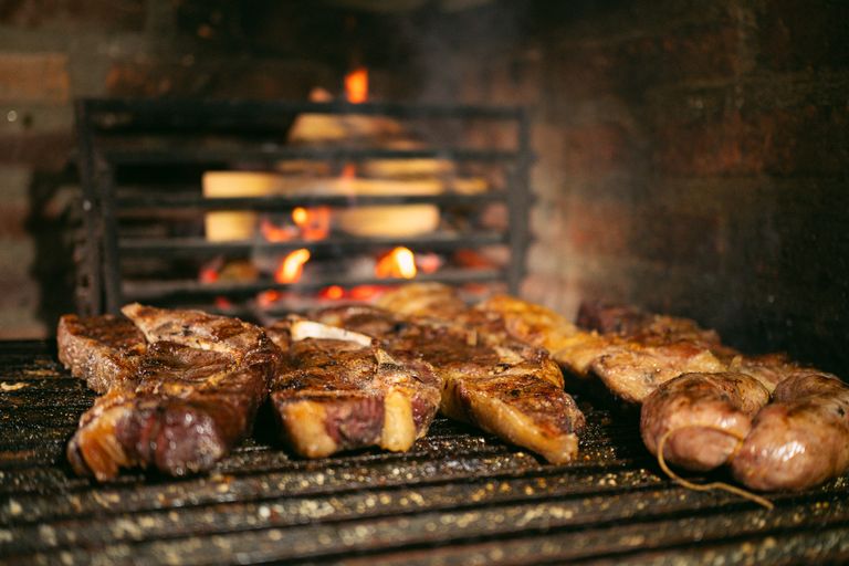 Delicious steaks and sausages sizzling on a grill with open fire background, perfect for barbecue lovers.