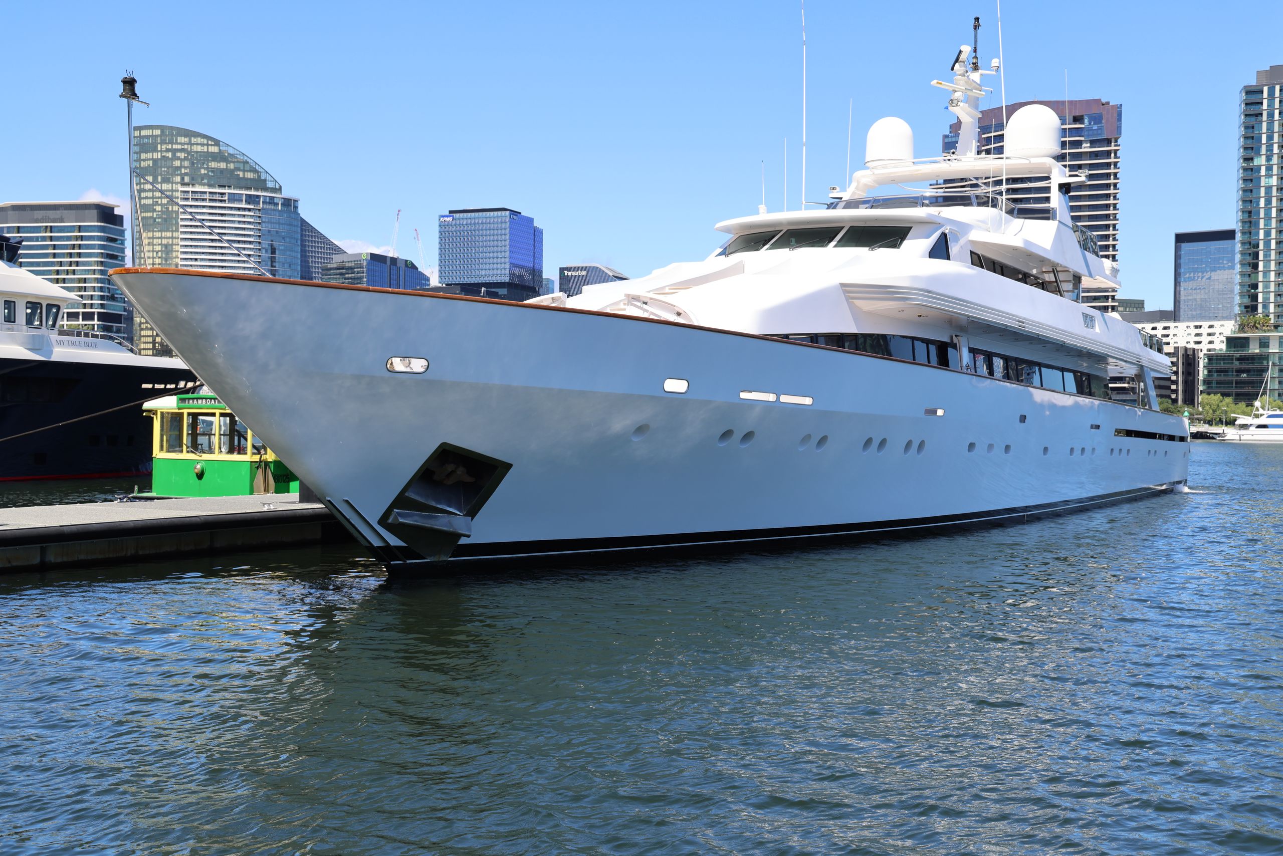 Large white luxury yacht docked at a modern urban marina with skyscrapers in the background.