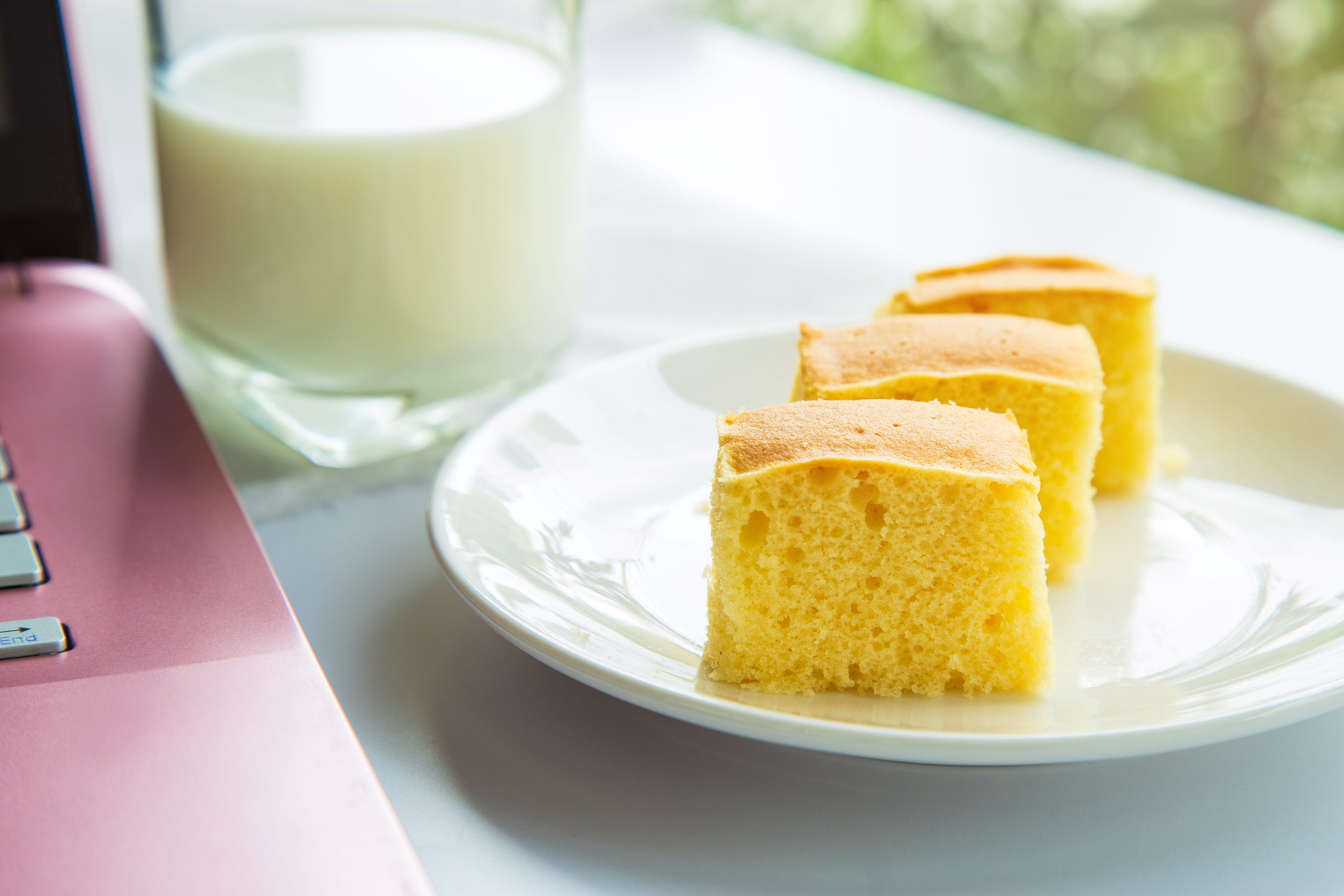 Close up a butter cake pack in a white plate next to a pink laptop device with a cup of milk blurred background in the afternoon.