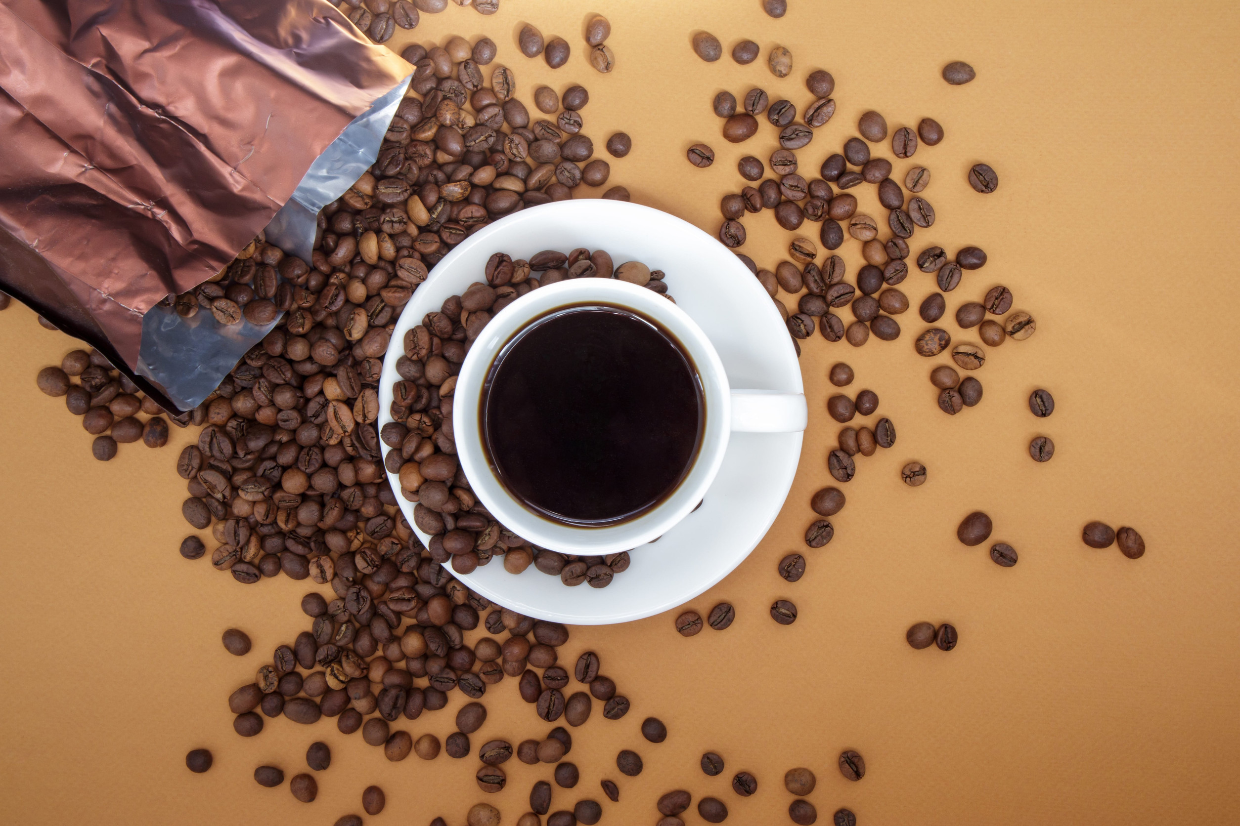 White cup of Americano black coffee without milk with a bunch of roasted coffee beans scattered from paper packaging. Coffee background, top view with copy space