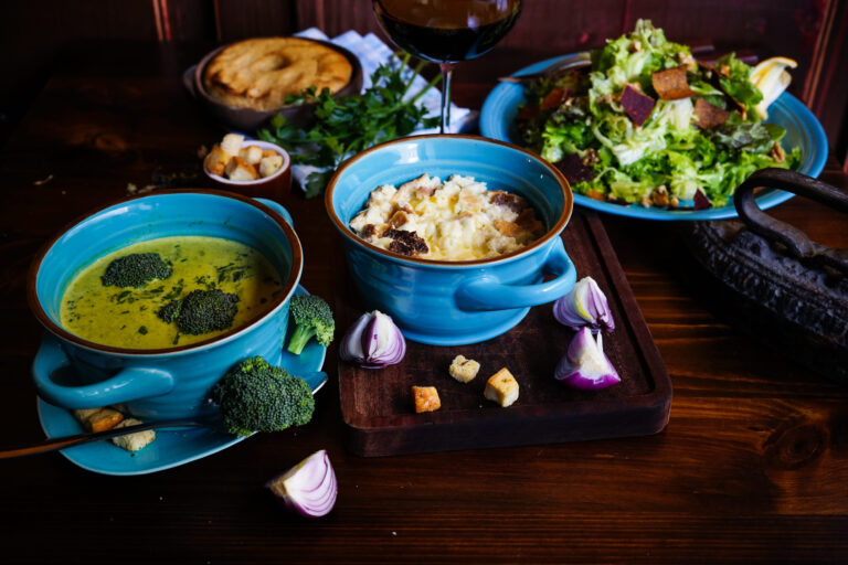Rustic dinner set with healthy broccoli cream soup, salad and corn milk porridge on dark wooden table