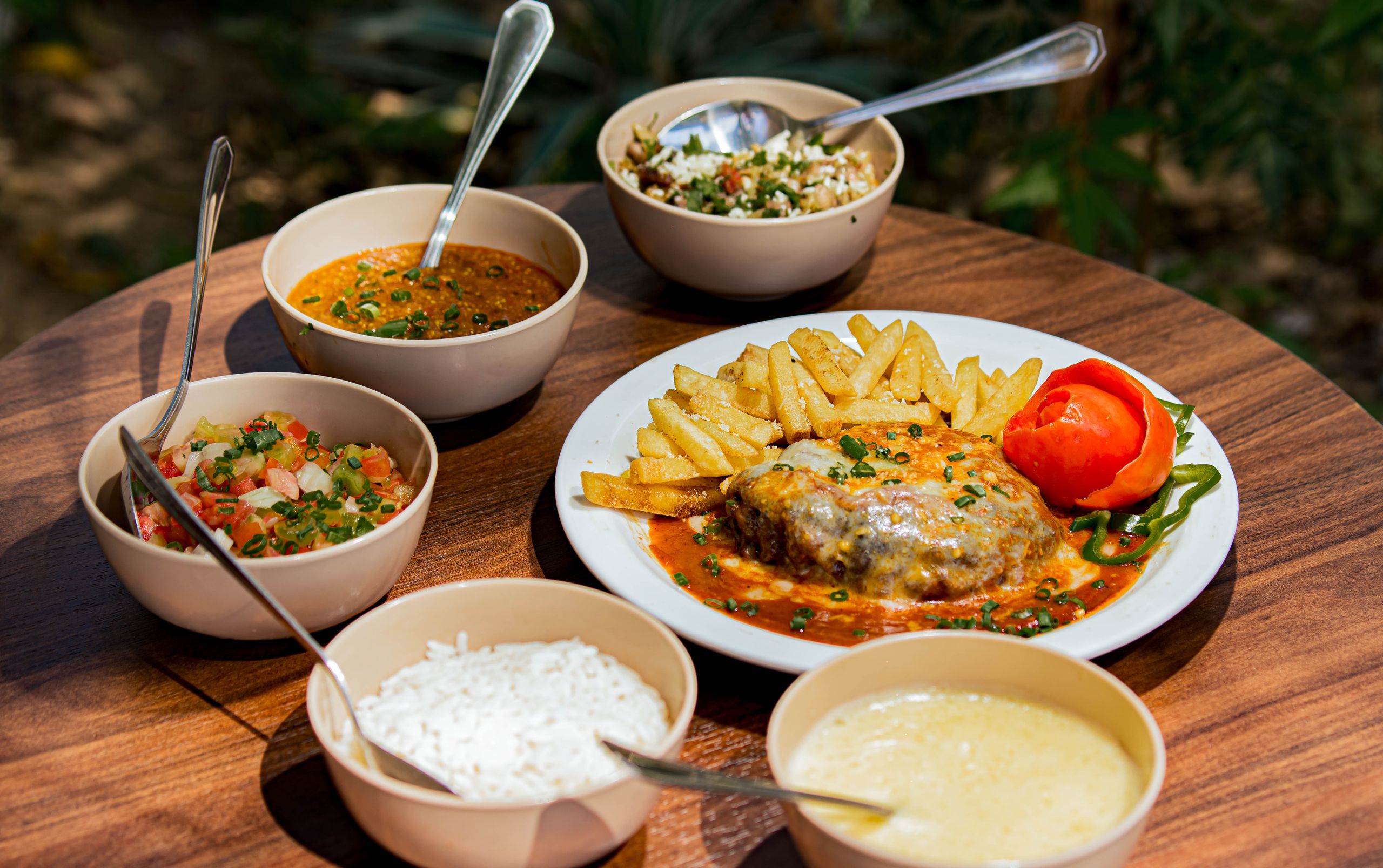 An appetizing display of mixed dishes including fries, salad, and rice on an outdoor wooden table.