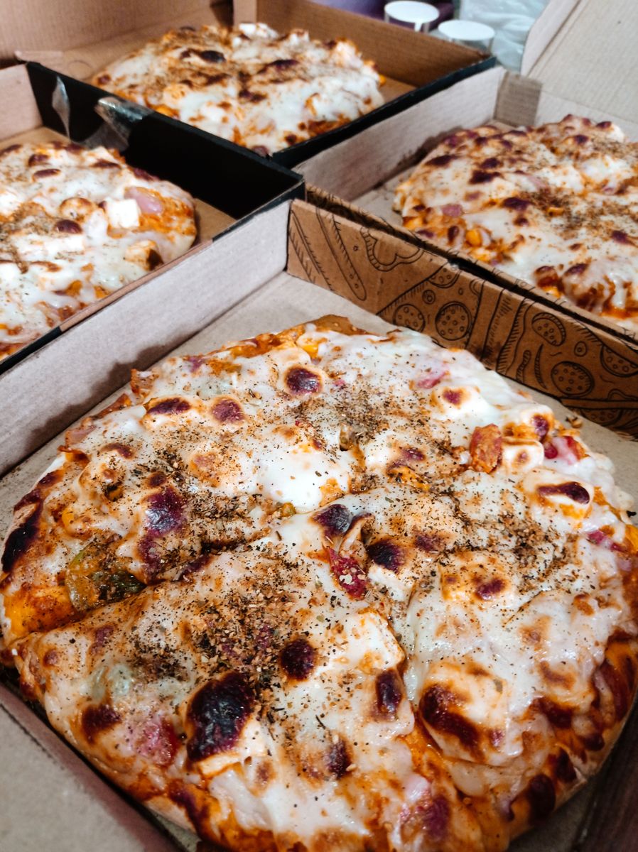 Close-up of freshly baked Italian pizzas in cardboard boxes, showcasing tempting toppings and melted cheese.