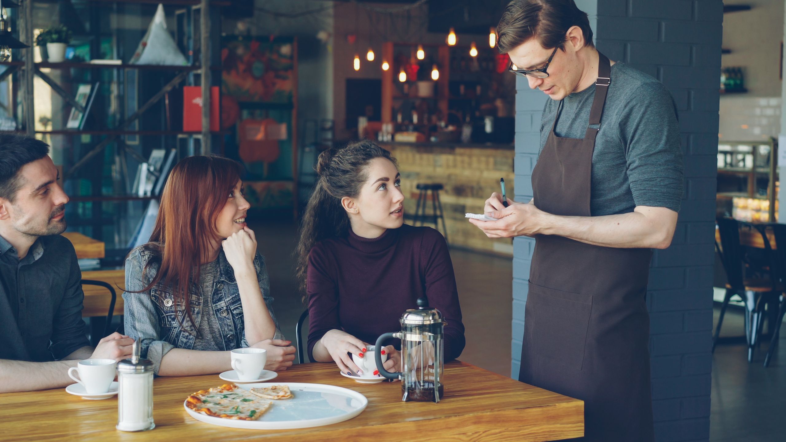 People having a relaxed meeting in a cozy caf&eacute;, interacting with a waiter.