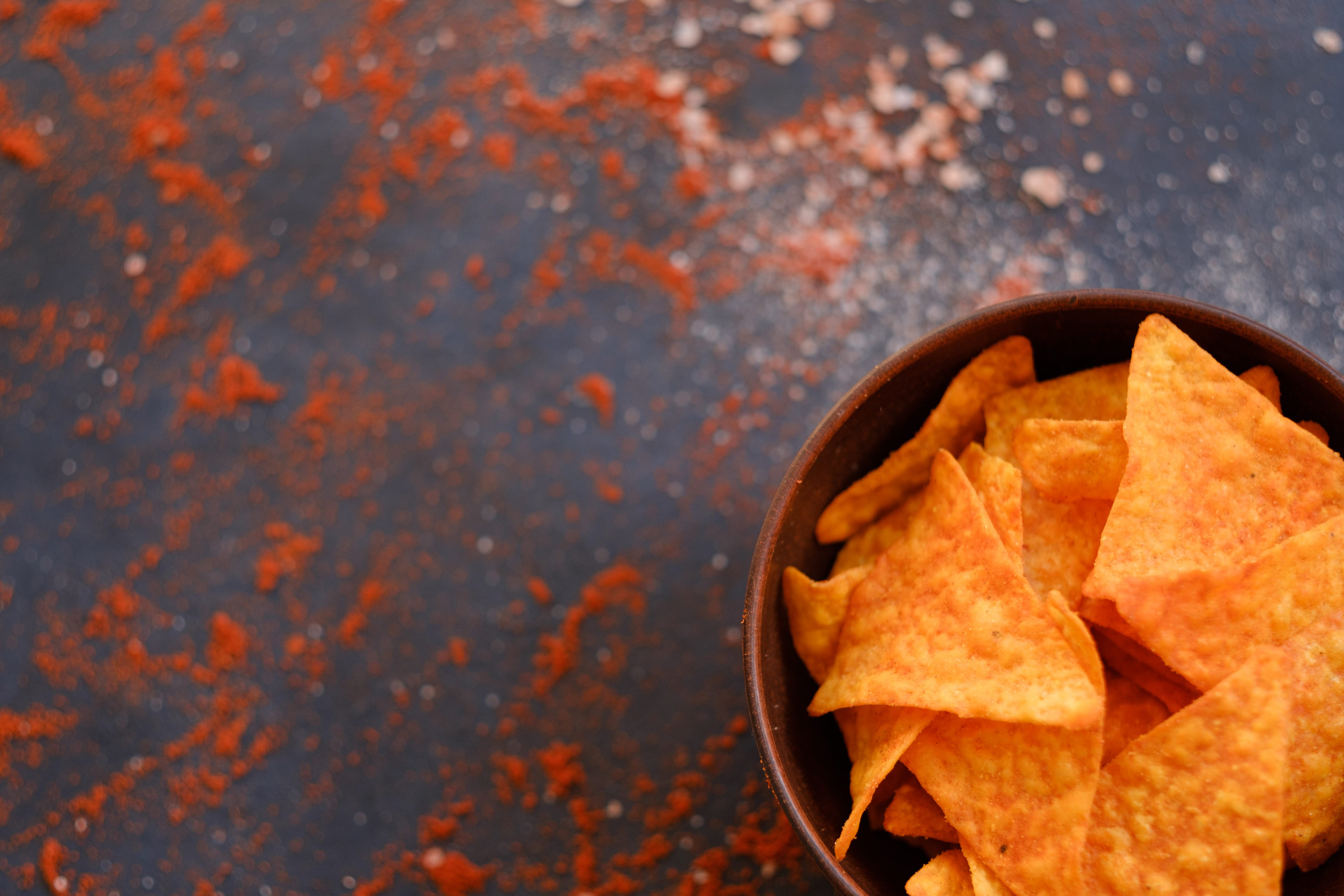 tortilla nacho chips in a bowl. food for quick snack. salt and powdered papriks spice mix on dark background