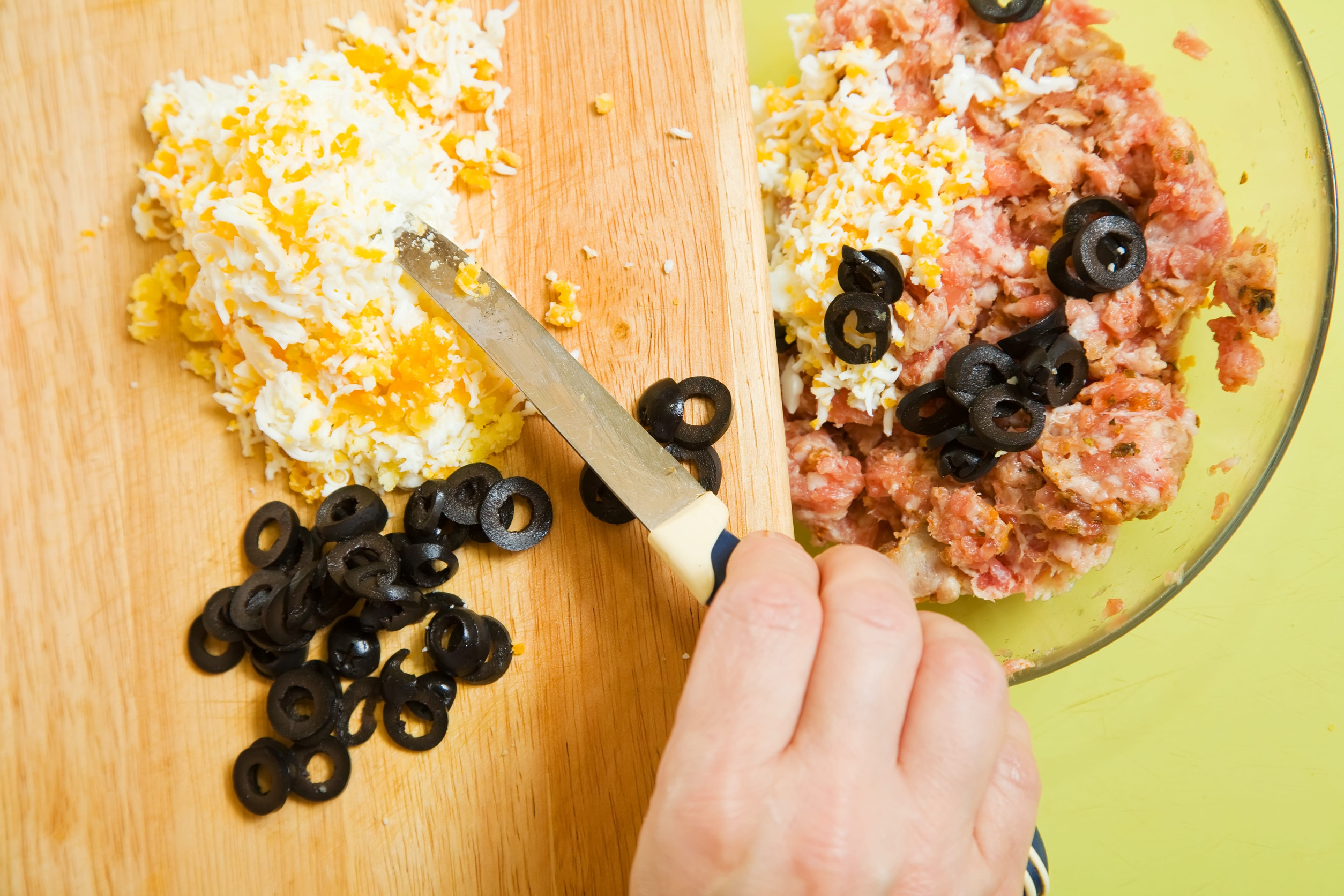 Closeup of adds grated eggs and sliced olives in mince. See in series stages of cooking of farci tomato