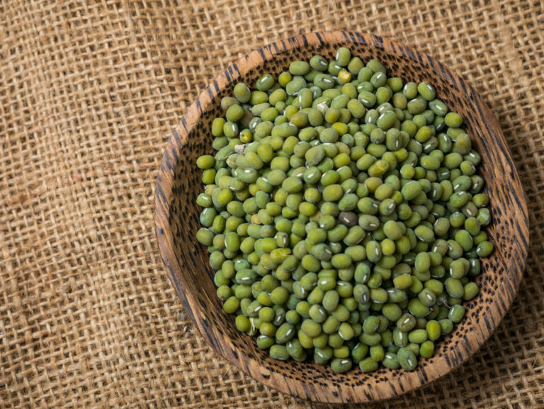 A rustic wooden bowl filled with fresh, vibrant green mung beans sits elegantly atop a textured burlap fabric, symbolizing nourishment and health. The beans’ natural sheen catches the light, inviting thoughts of culinary creativity and wholesome meals. Image Credit: airdone/ 123RF