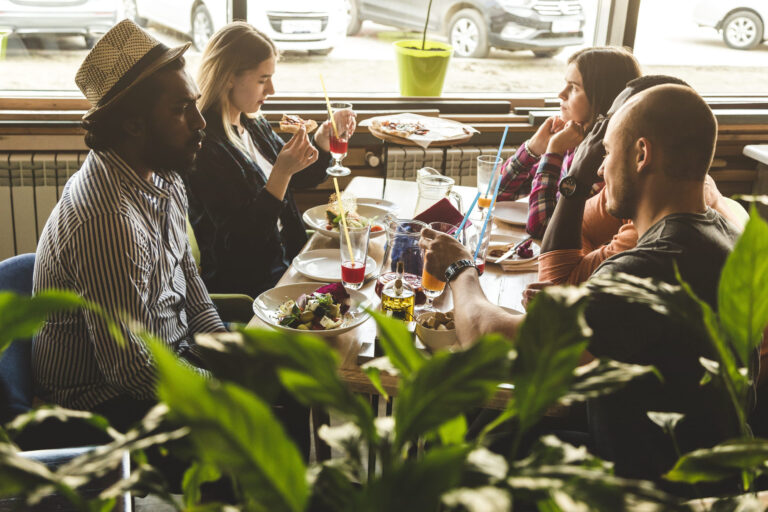 A company of multicultural young people in a cafe eating pizza, drinking cocktails, having fun