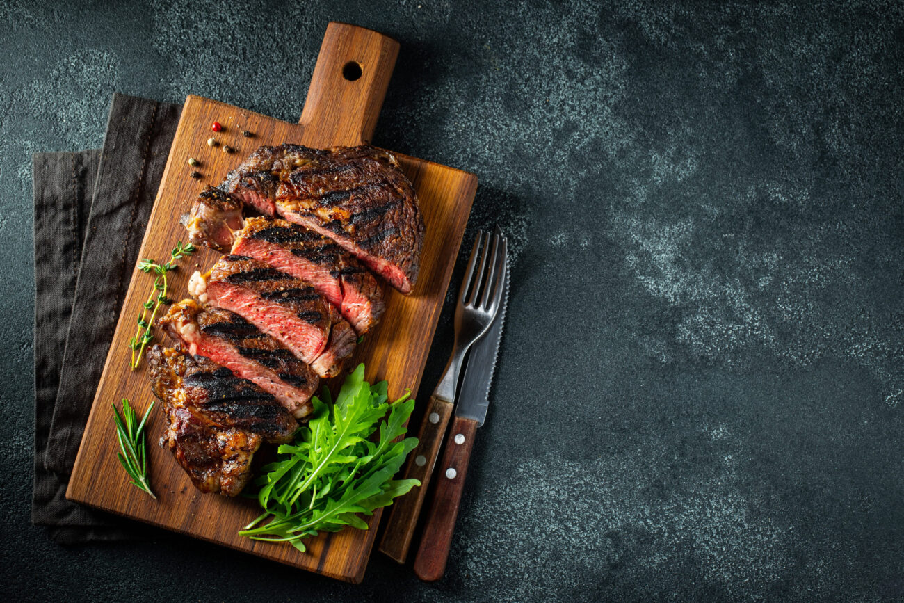 A perfectly grilled steak, beautifully sliced and elegantly presented on a rustic wooden board. Accompanied by fresh herbs, this dish showcases the art of culinary mastery, inviting you to savor every bite. Image Credit: vasiliybudarin/ 123RF