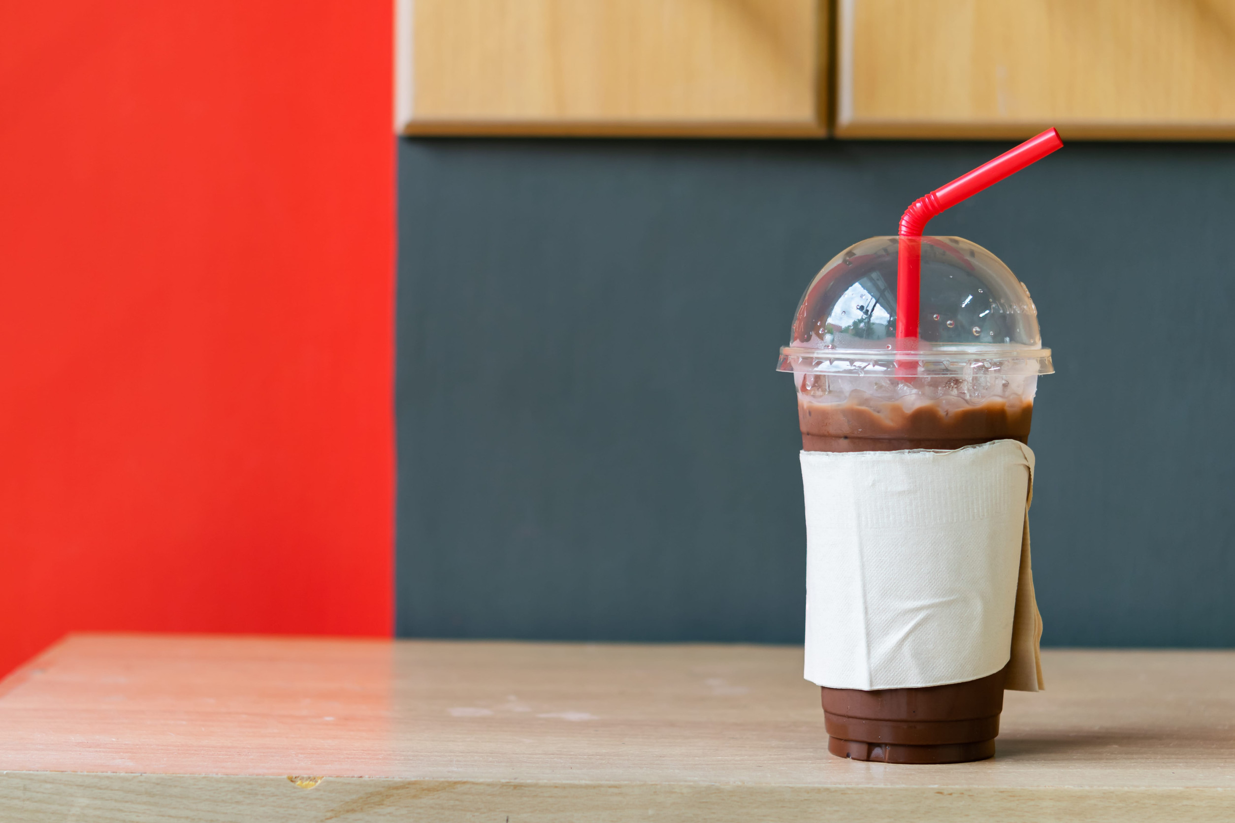 A glass of iced cocoa drink wrapped by brown tissue paper on the table