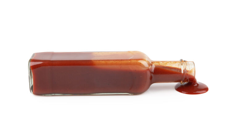 bottle of hot sauce is spilling liquid on white background