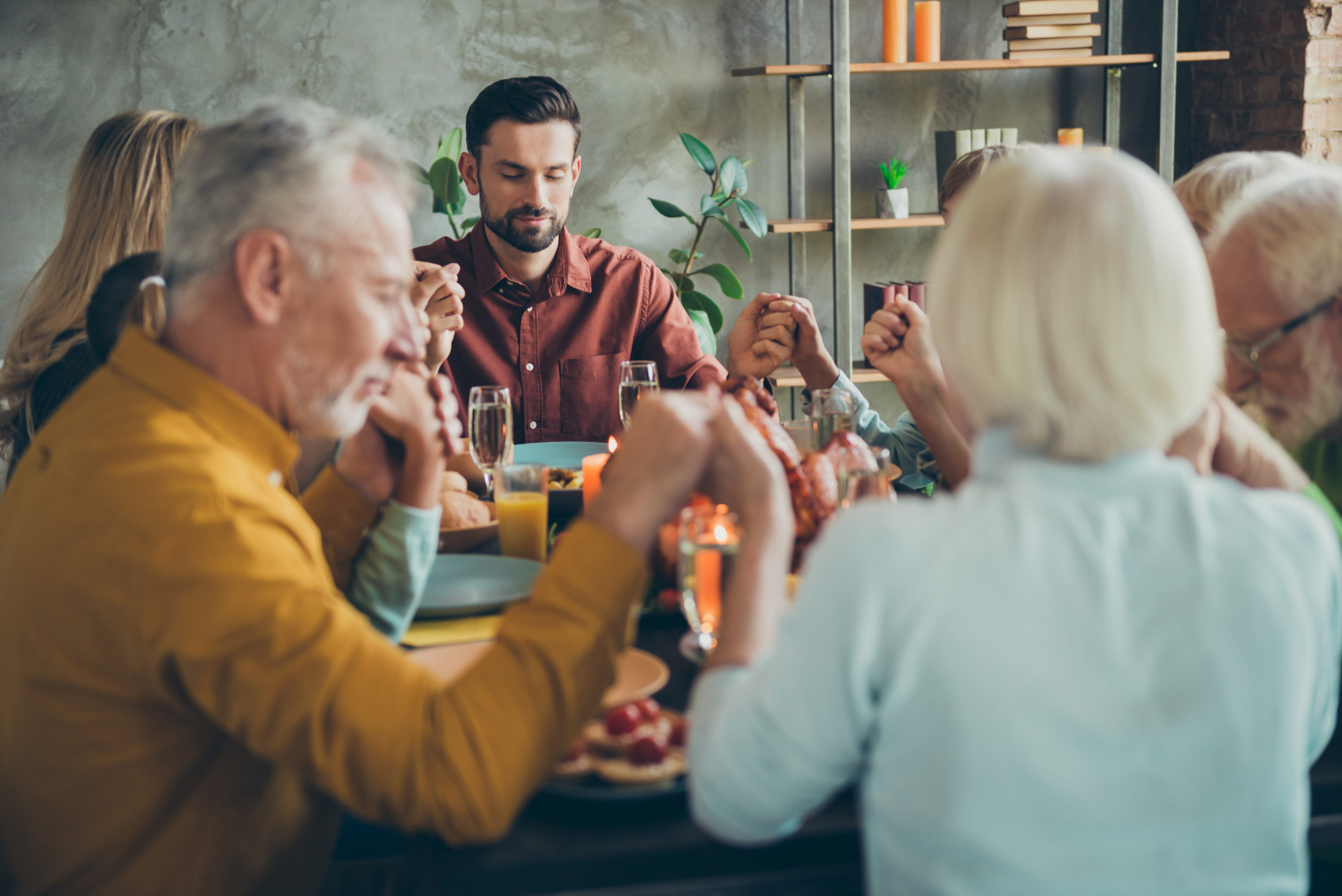 Big family of mature father mother small boy little girls pensioner celebrate fall october feasting holiday thanksgiving day pray sit table with chicken wine candles decoration in house