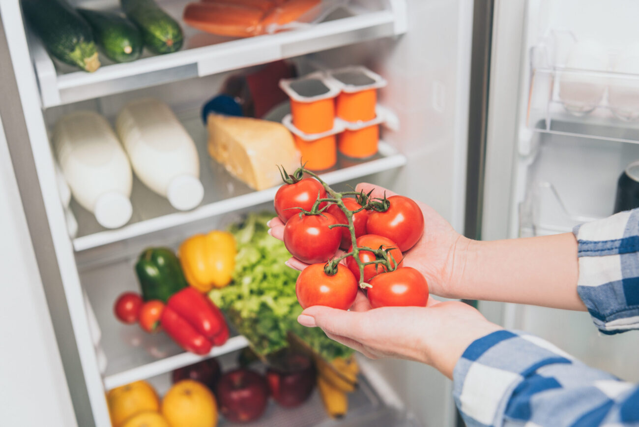 A home cook selects fresh tomatoes from a well-stocked refrigerator, ready to prepare a delicious meal. Image Credit: lightfieldstudios/ 123RF