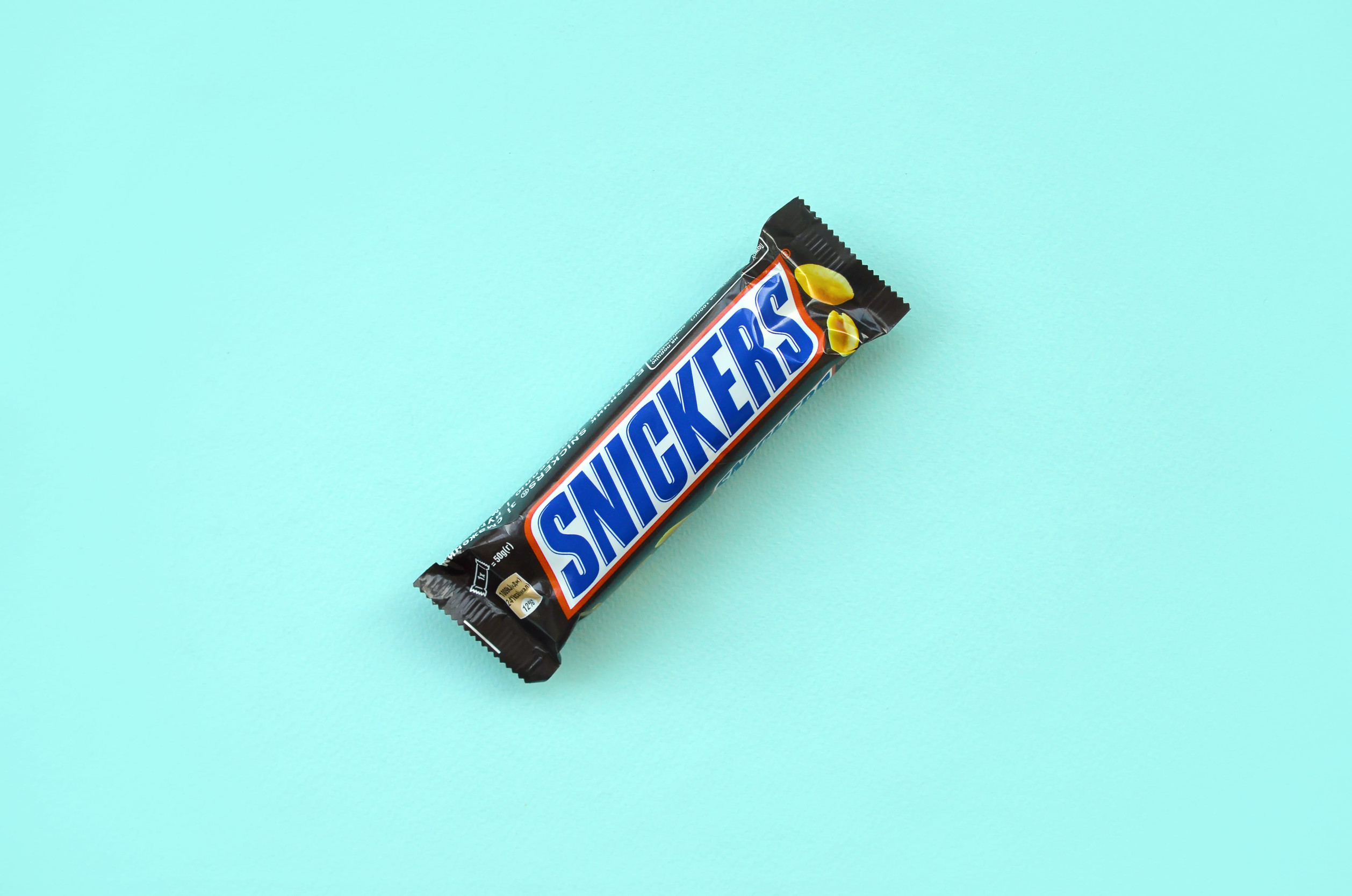 KHARKOV, UKRAINE - OCTOBER 2, 2019: Many Snickers chocolate bars lies on pastel blue paper. Snickers bars are produced by Mars Incorporated. Snickers was created by Franklin Clarence Mars in 1930