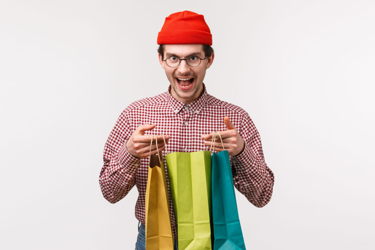 Excitement fills the air as a cheerful man showcases his vibrant shopping bags, ready for a fun-filled day of retail therapy and adventure. His playful expression and colorful bags reflect the joy of discovering new treasures amidst the hustle and bustle of the city. Image Credit: benzoix/ 123RF