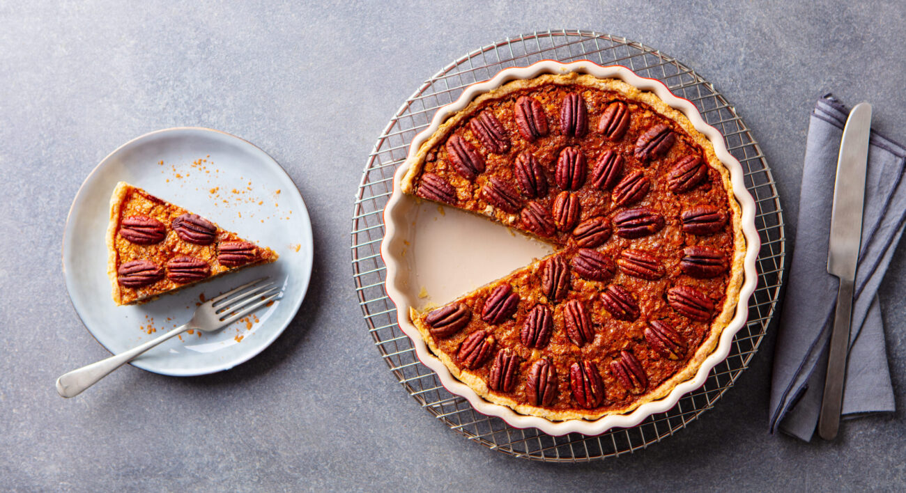 Indulge in a delightful pecan pie, beautifully arranged with perfectly roasted pecans atop a rich, caramel-filled filling. A tantalizing slice sits nearby, inviting you to savor its sweet, nutty goodness, perfect for any gathering or special occasion. Image Credit: annapustynnikova/ 123RF
