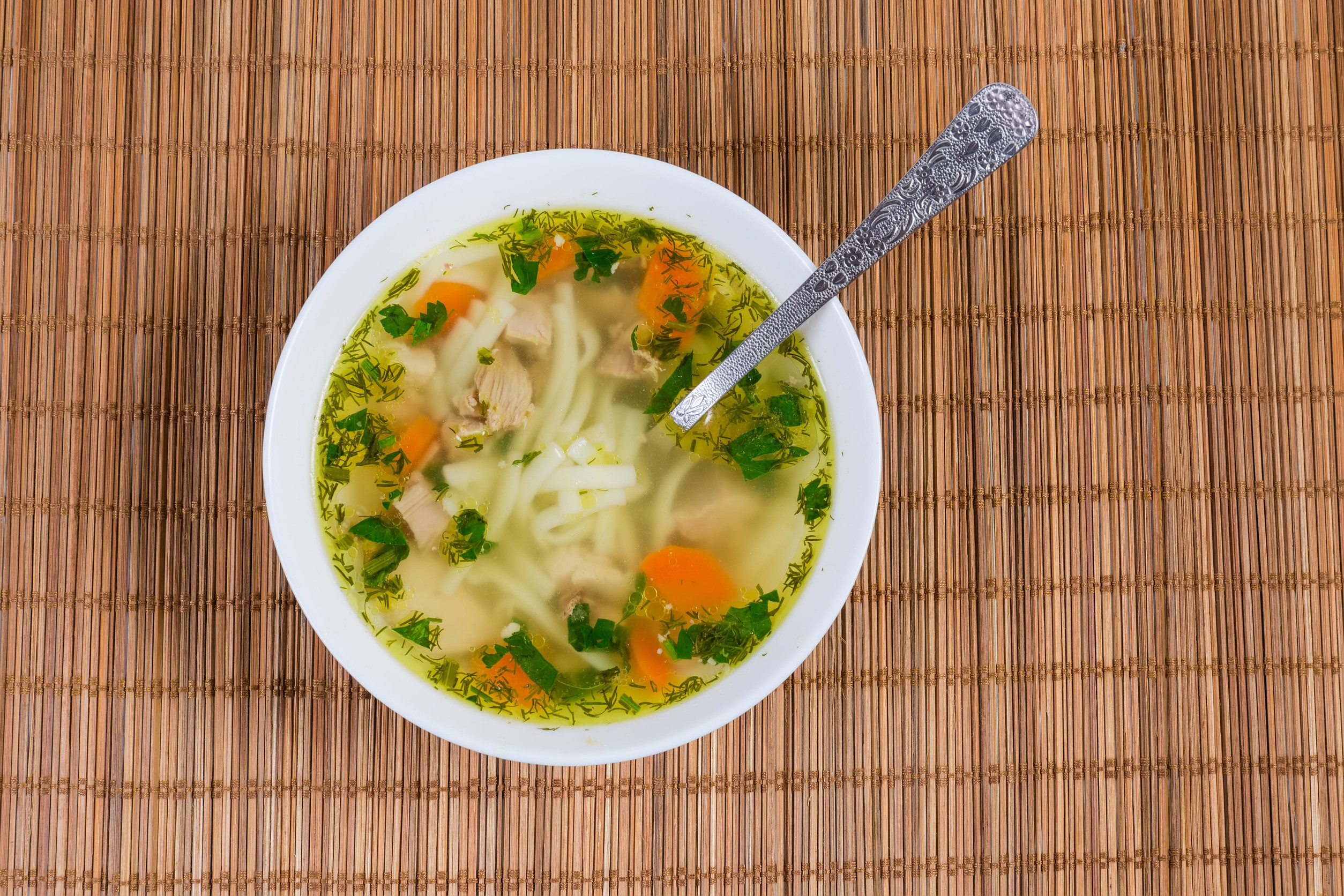 Comforting Noodle Recipes You Need to Try 1 Homemade chicken soup with noodle in the white bowl with spoon on the bamboo table mat, top view