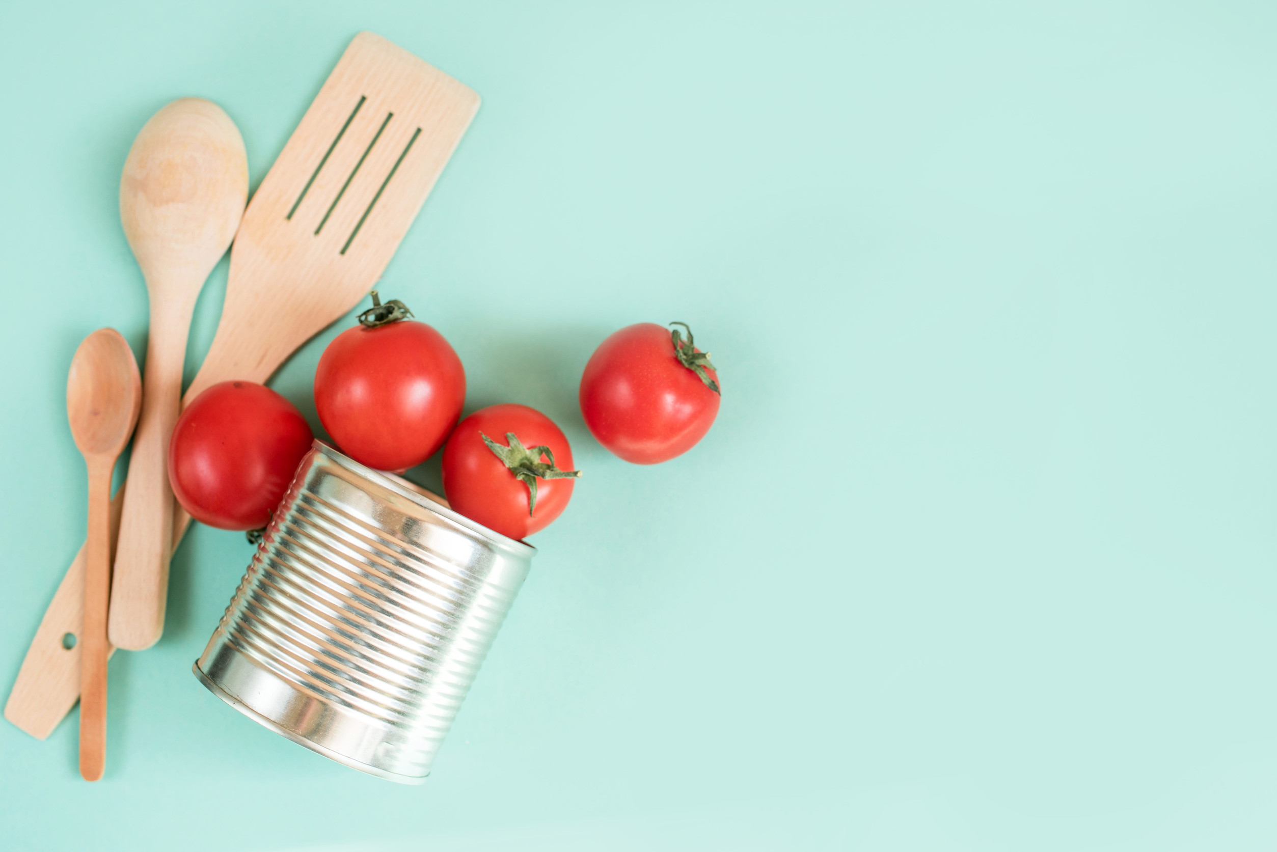 Tree spatula and spoons, ripe tomatoes, and a can of tin with food lie on a light background. View from above, place for inscription.