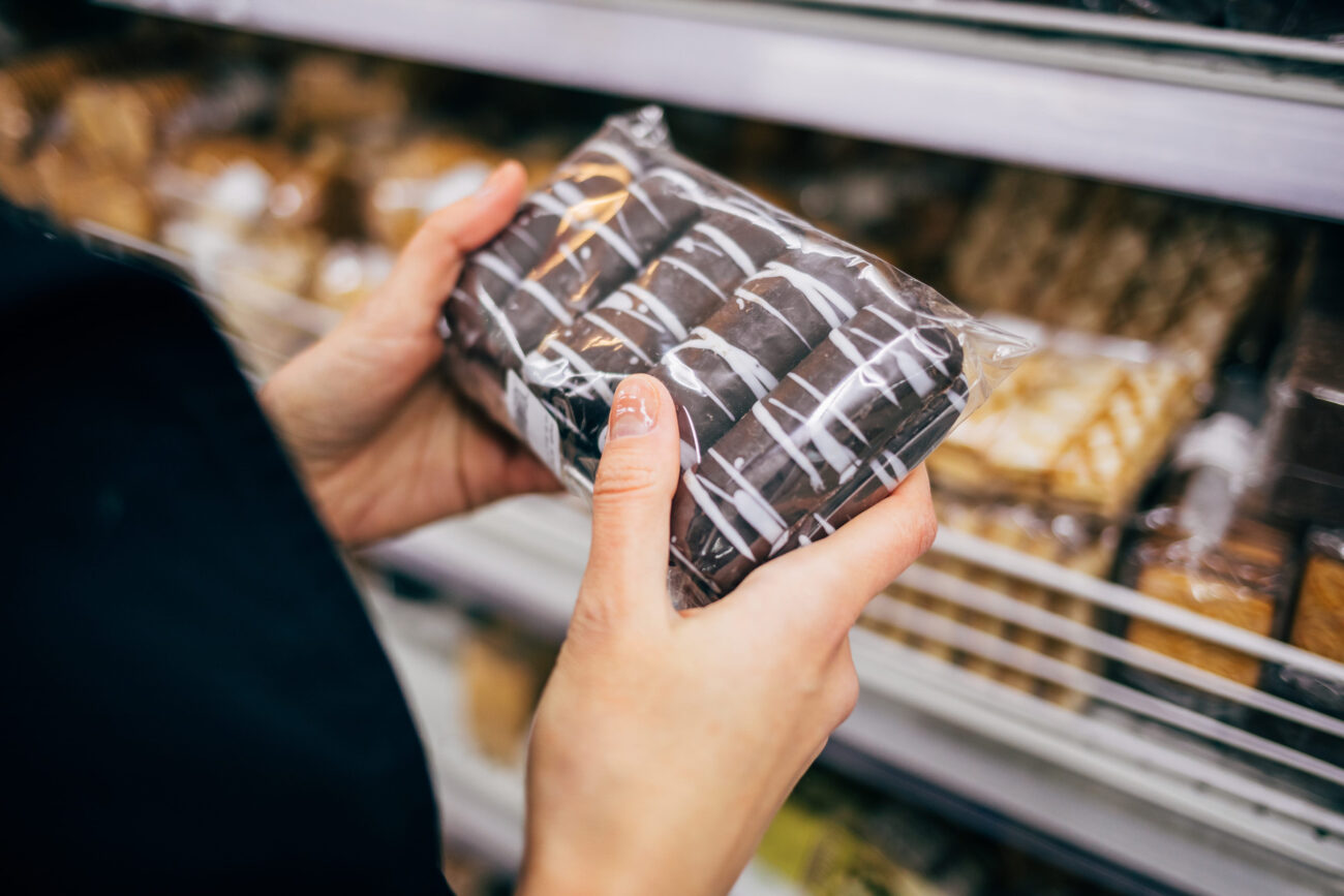A curious shopper carefully examines a beautifully wrapped package of delectable treats, contemplating the sweet indulgence that lies within. Each layer of chocolate and cream beckons with the promise of a delightful experience, capturing the essence of everyday joys found in simple pleasures. Image Credit: progressman/ 123RF