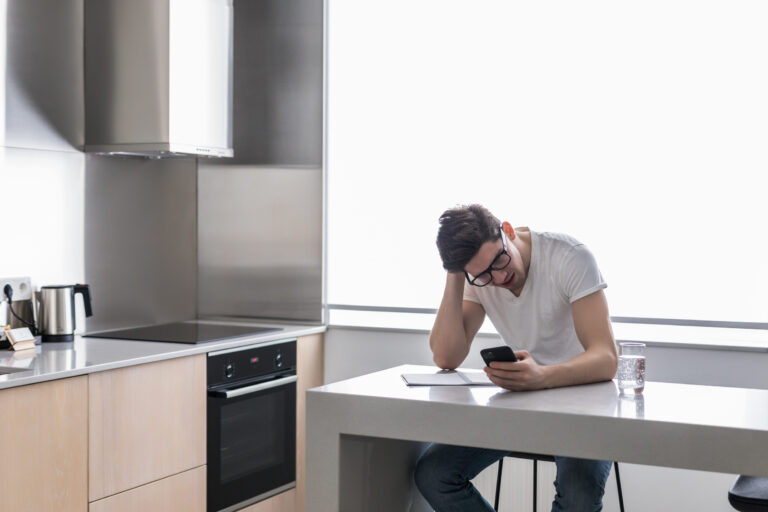 Worried man looking at phone in the kitchen