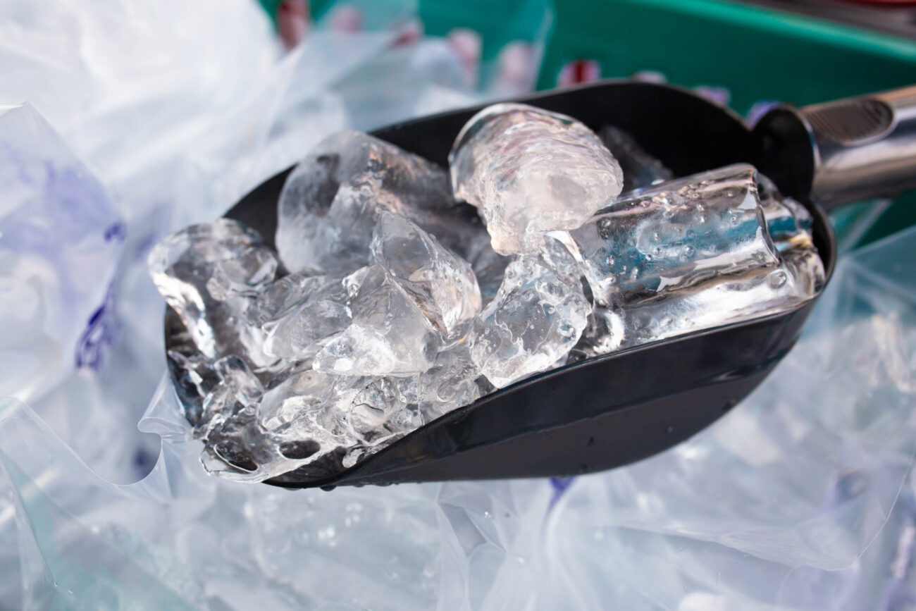 A gleaming scoop filled with crystal-clear ice cubes sits atop a bed of crushed ice, capturing the essence of freshness and chill in the bustling heat of a summer market. Image Credit: macmackyky/ 123RF