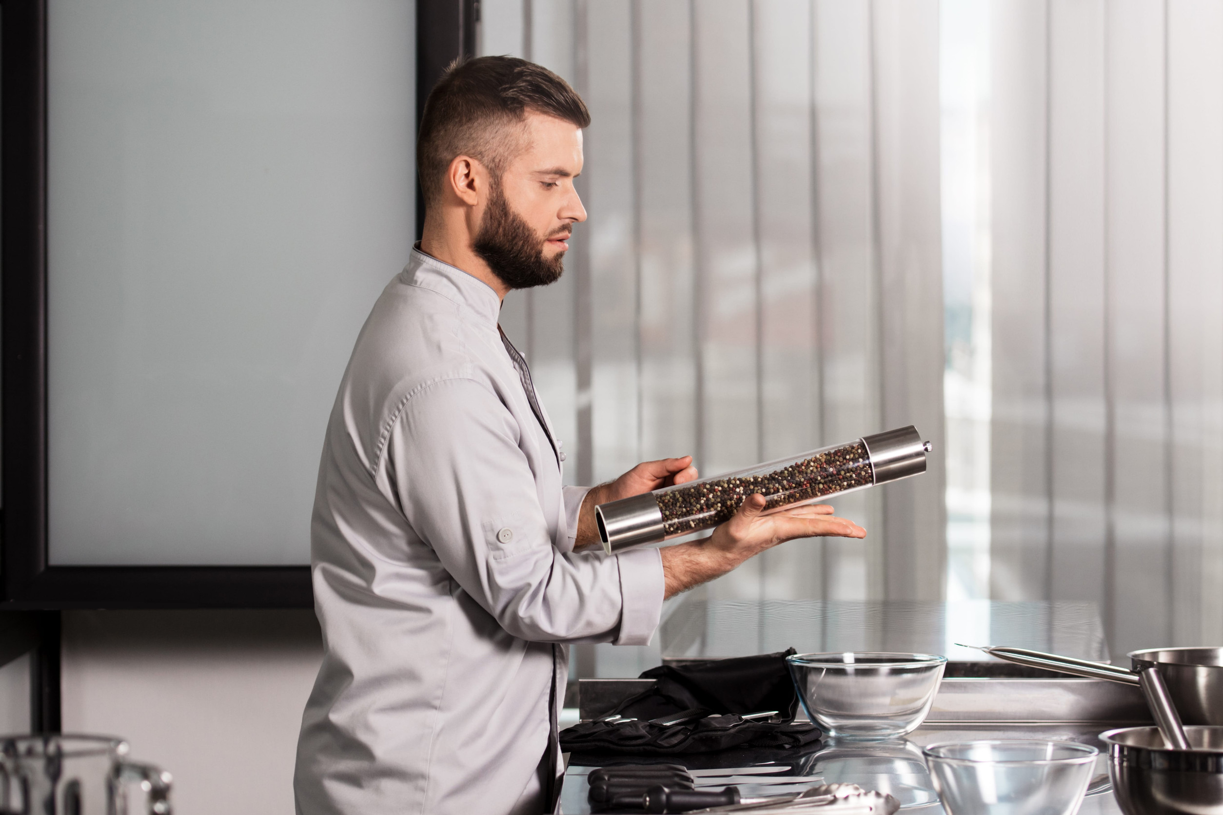 Chef man with pepperbox at kitchen. Portrait of cook with pepperbox. Male professional in uniform posing with pepperbox at restaurant kitchen.