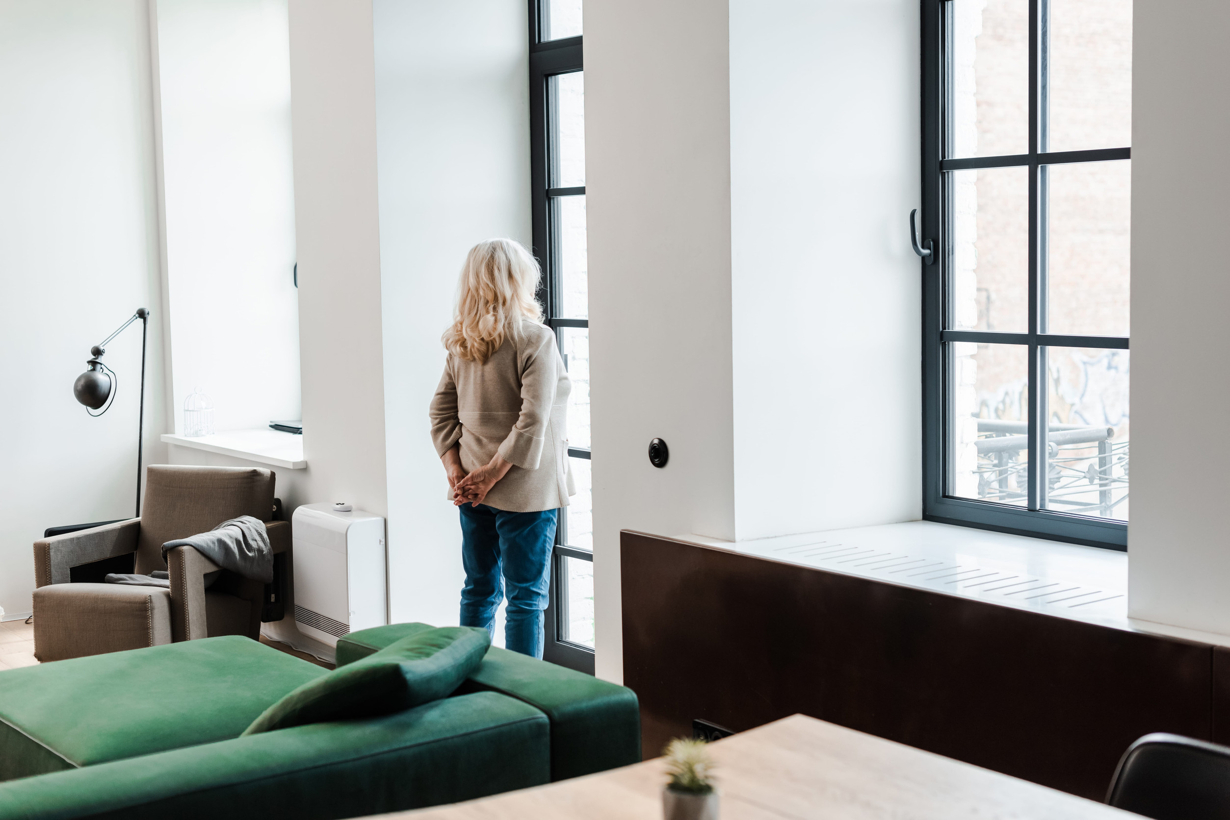 upset senior woman standing near window at home during quarantine