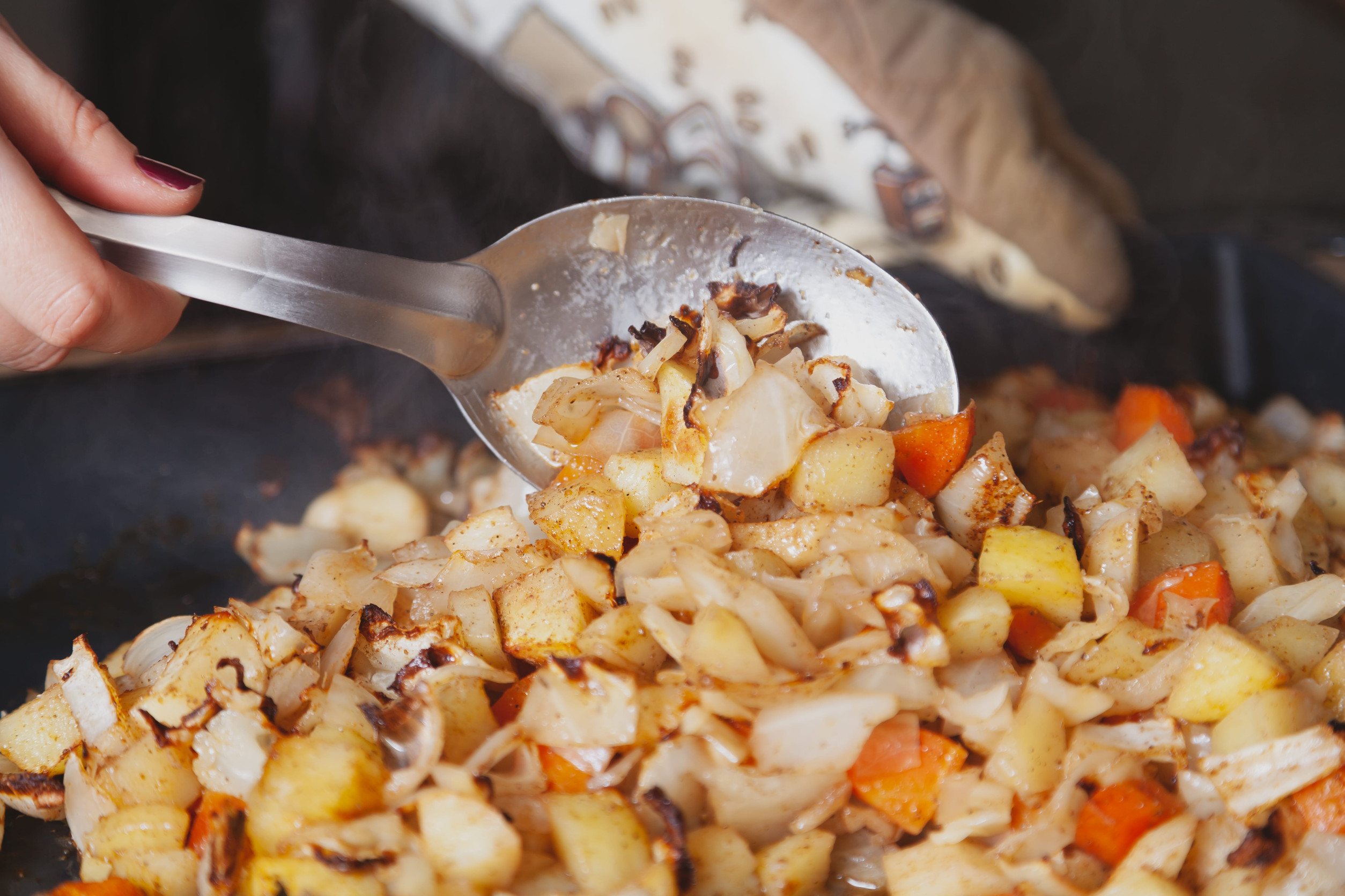 Appetizing vegetable stew. Large steel spoon stirs baked vegetables in a metal baking sheet