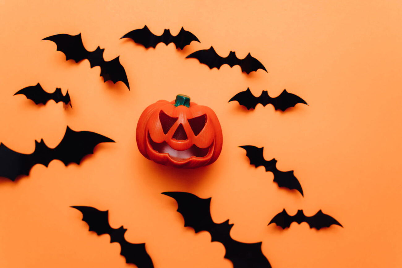 A playful Halloween scene featuring a grinning jack-o'-lantern surrounded by cute bat cutouts. The vibrant orange background adds a festive flair, perfect for spooky celebrations. Image Credit: etonastenka/ 123RF