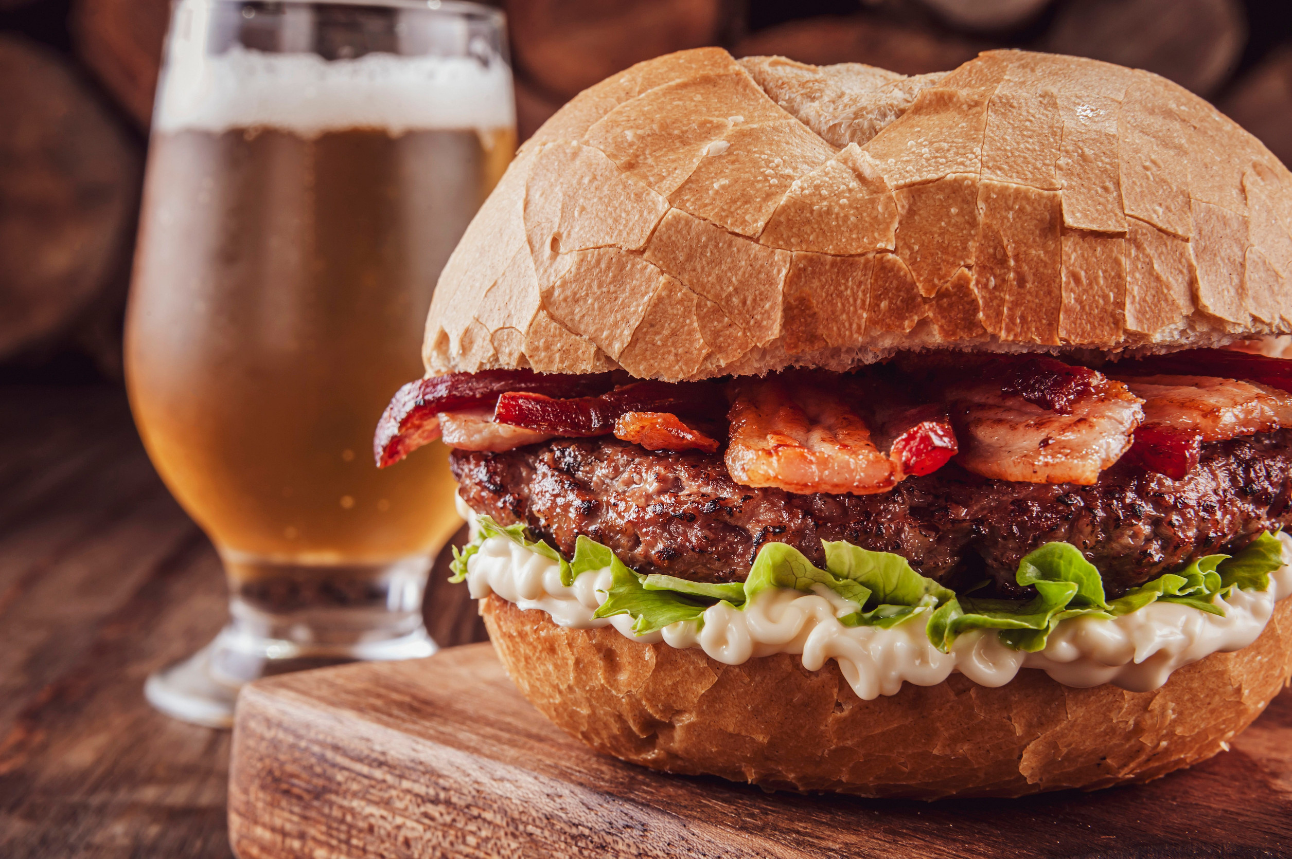 Bacon burger with a glass of beer and firewood pile in background - Close-up