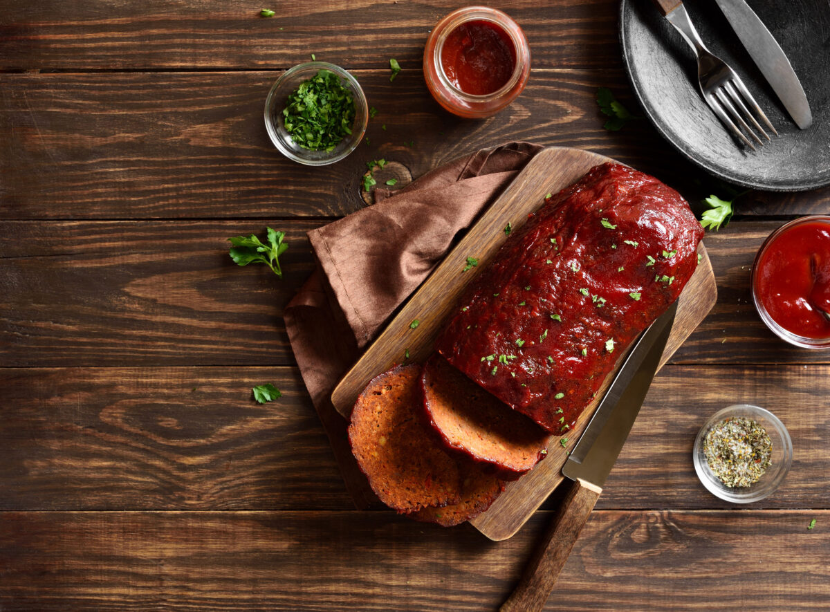 A deliciously cooked meatloaf crafted with care, garnished with fresh herbs and presented on a rustic cutting board, accompanied by a rich tomato sauce and a side of crispy potato slices, perfect for a cozy family dinner. Image Credit: voltan1/ 123RF