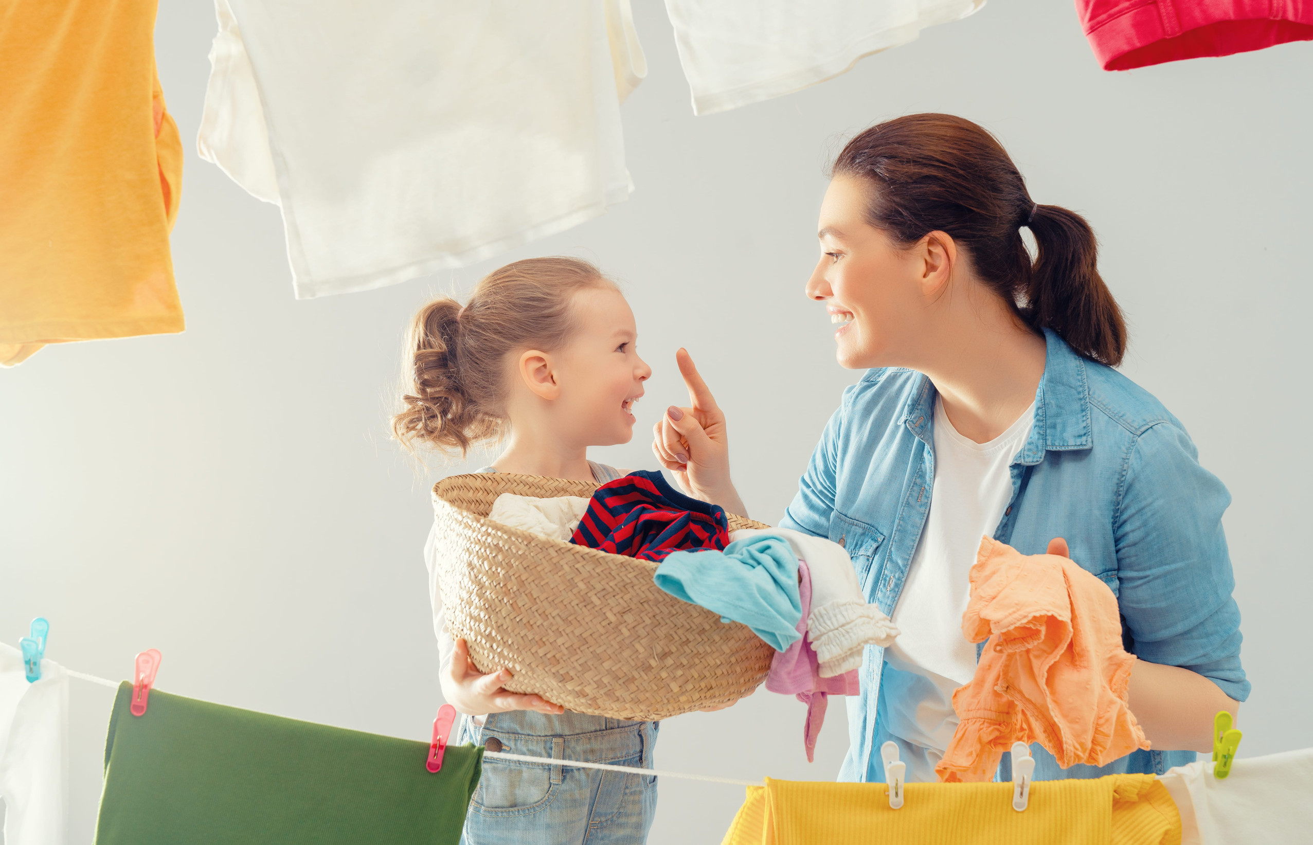 Beautiful young woman and child girl little helper are having fun and smiling while doing laundry and drying.