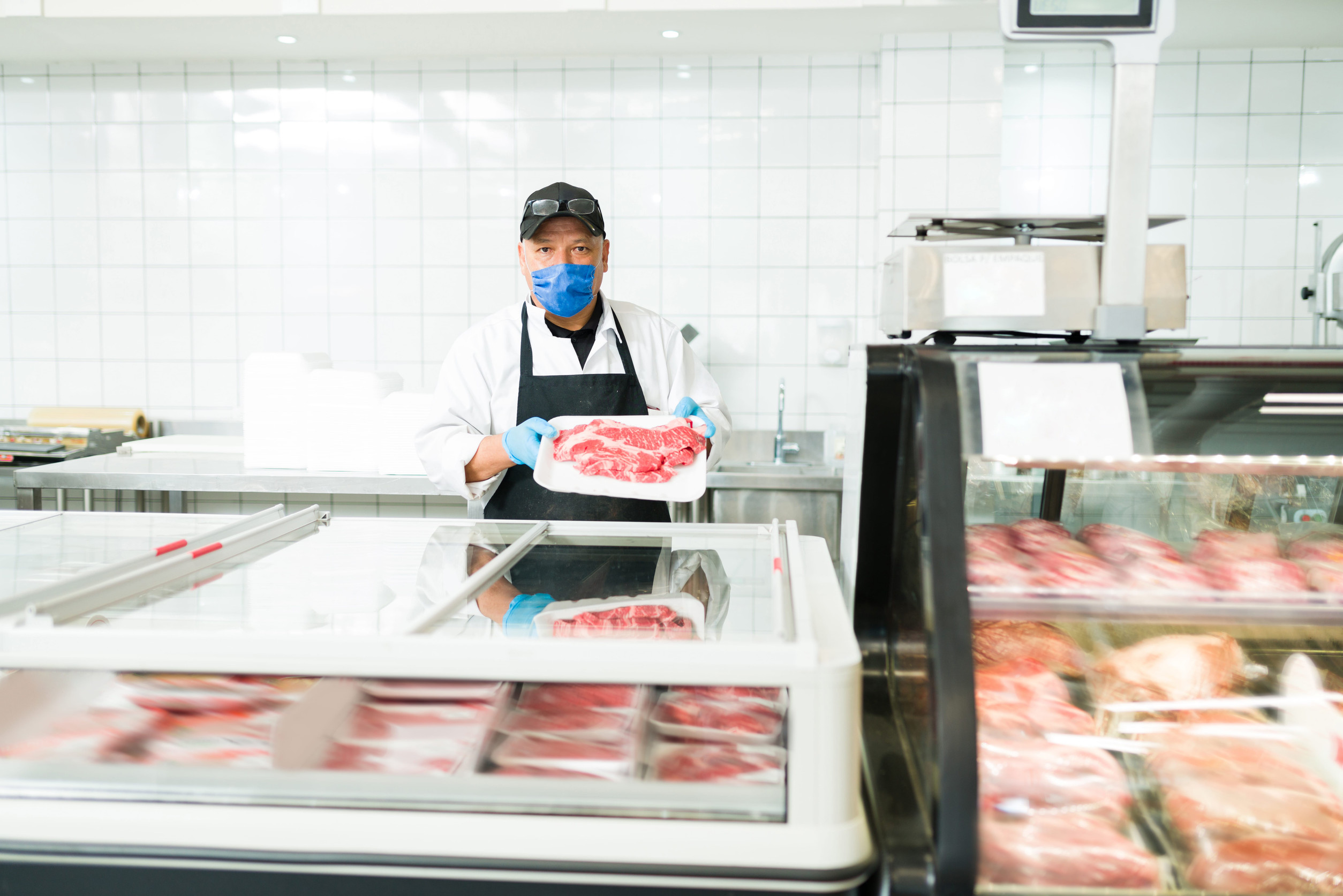 Male salesman using a face mask while working at a butcher shop. Portrait of a worker at the supermarket selling raw meat