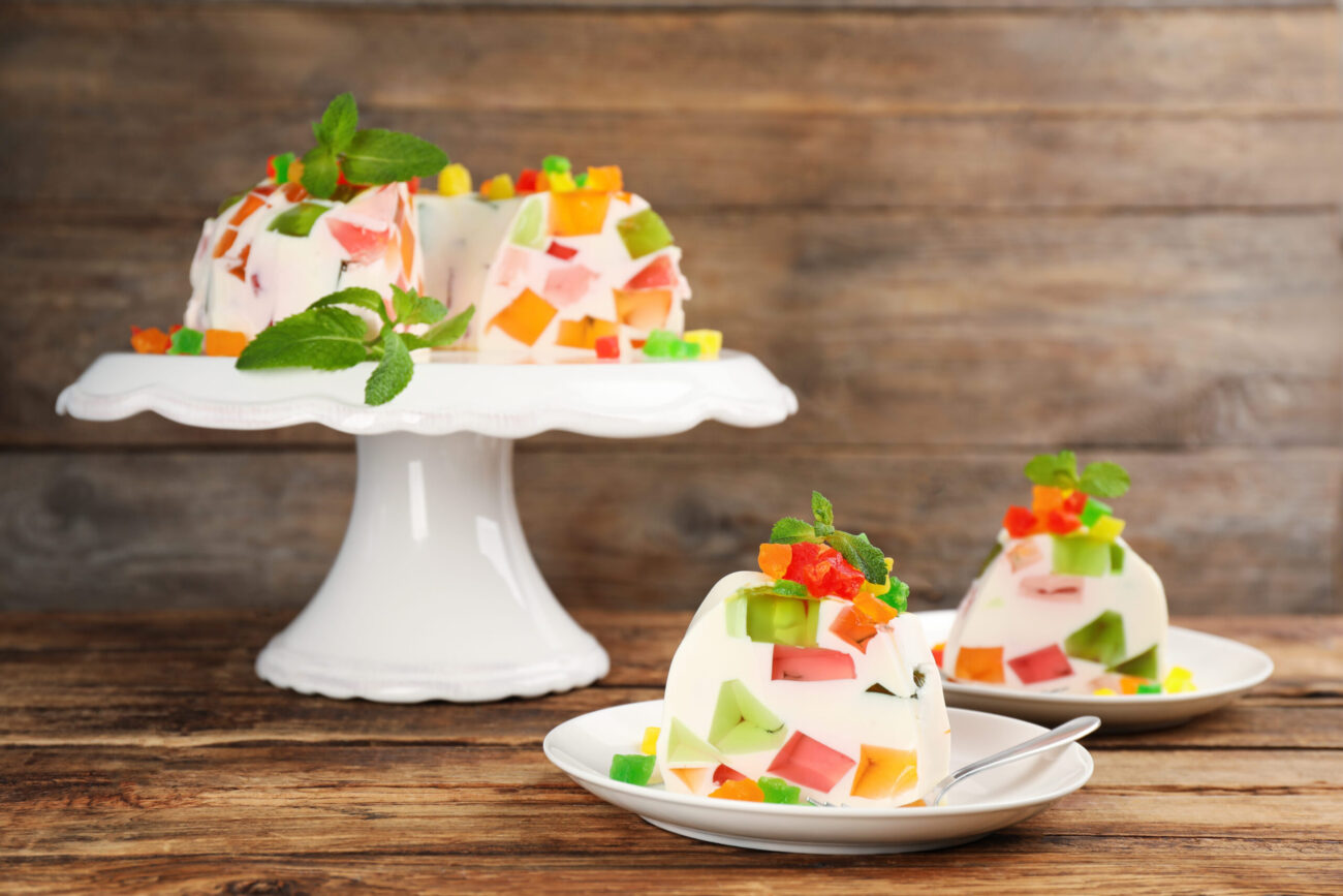 A delightful display of colorful jelly desserts adorned with fresh mint leaves, resting elegantly on a white cake stand, inviting guests to indulge in a sweet treat filled with vibrant flavors and textures. Image Credit: liudmilachernetska/ 123RF