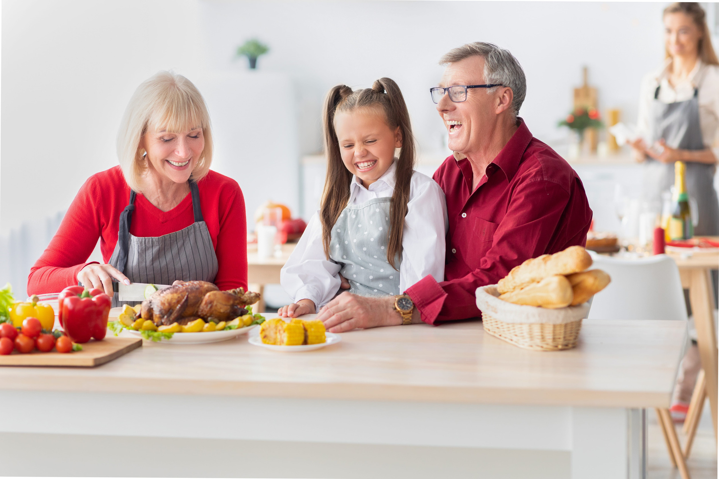Cheerful girl with her grandparents cooking traditional festive dinner together, preparing roast turkey for family meal