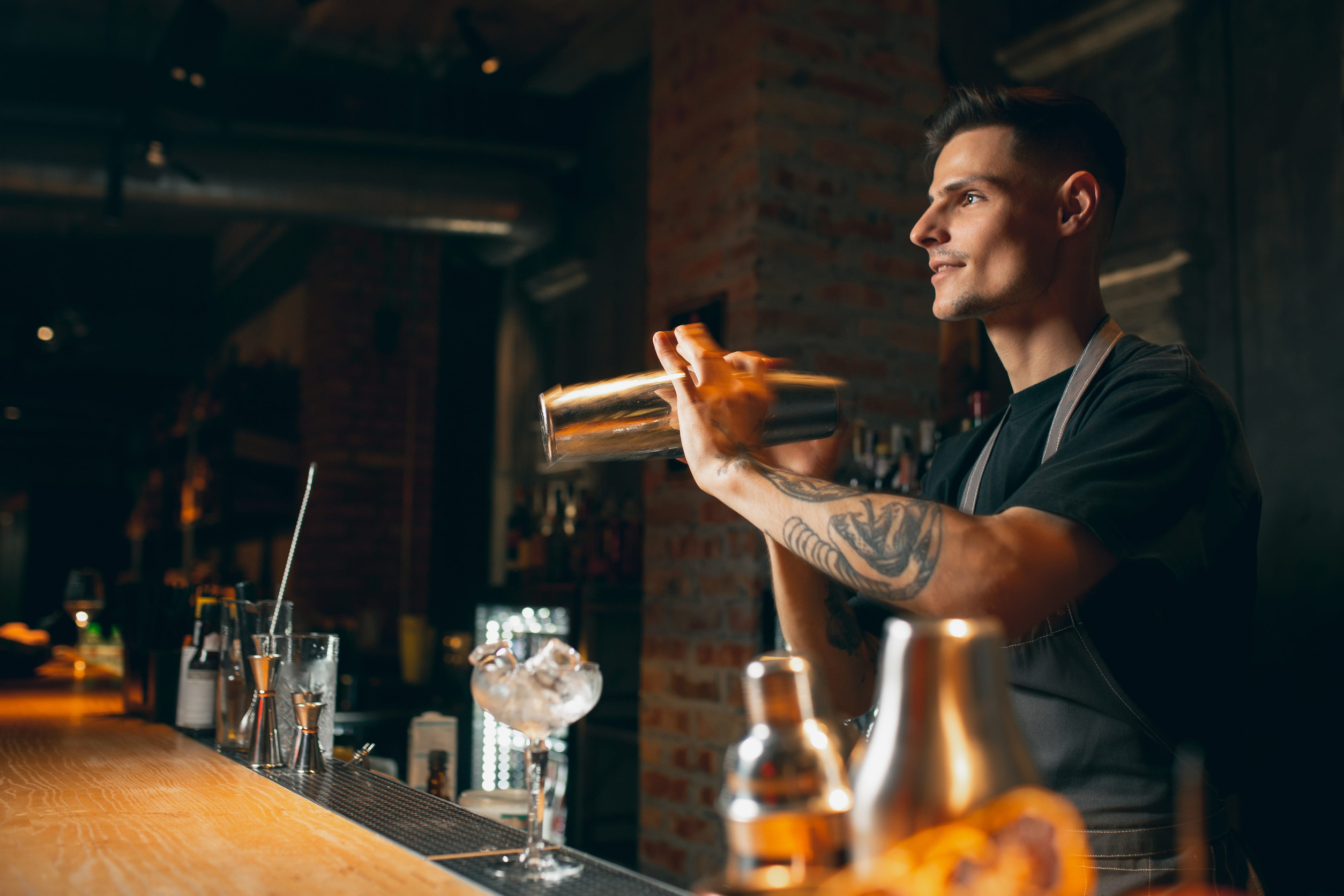 Shaking, mixing. One professional bartender shaking an alcohol drink in cocktail shaker enjoying his job. Side view