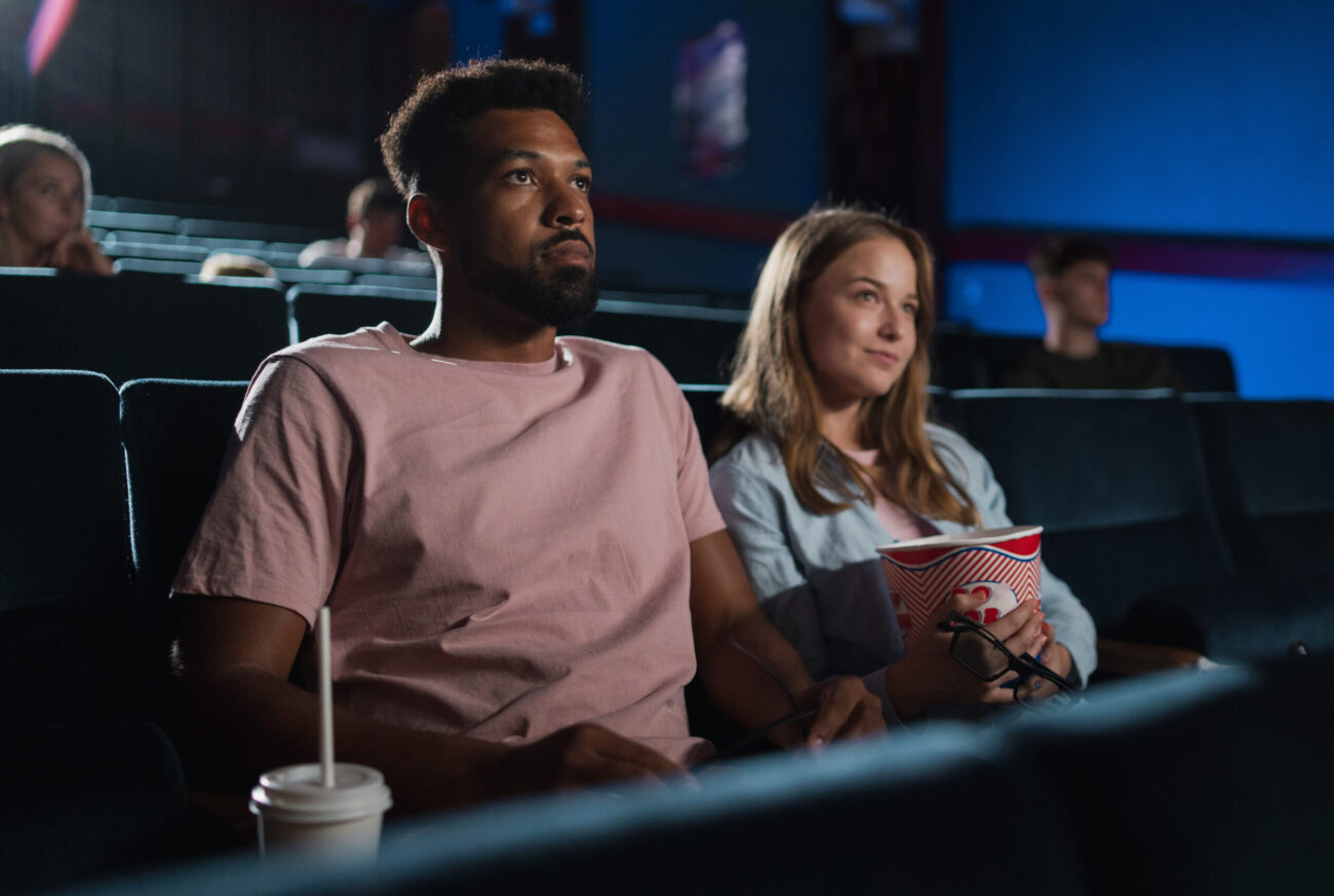 In a cozy movie theater, a young couple enjoys an evening of entertainment, sharing popcorn and laughter as the film unfolds. The soft glow of the screen illuminates their faces, creating a warm and inviting atmosphere perfect for a romantic night out. Image Credit: halfpoint/ 123RF