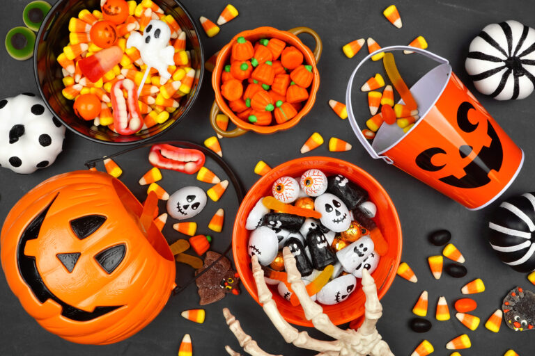 Candy corn, gummy candies, and fun-shaped chocolates await eager trick-or-treaters, inside vibrant orange bowls and containers shaped like pumpkins. Image Credit: jenifoto/ 123RF