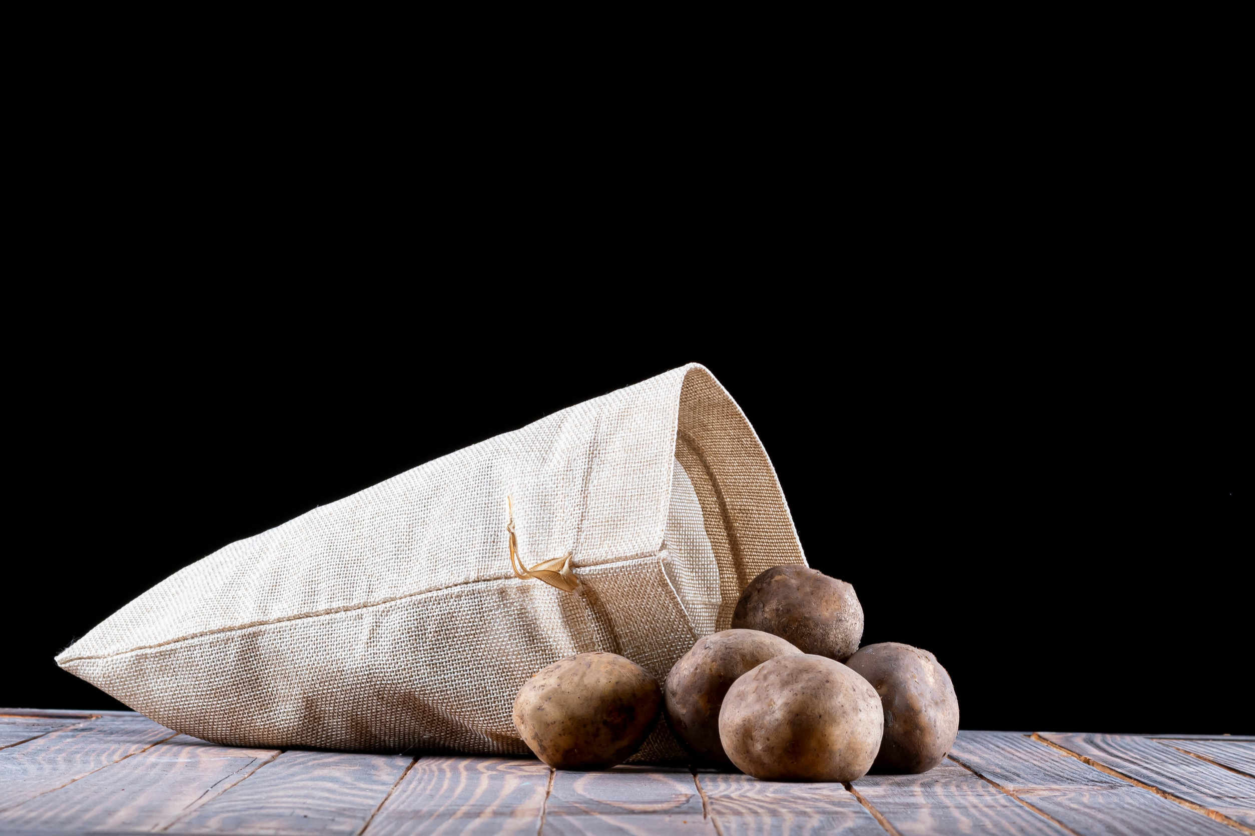 studio lighting. black background. potatoes are planted from a bag on a retro-style wooden background. close-up.