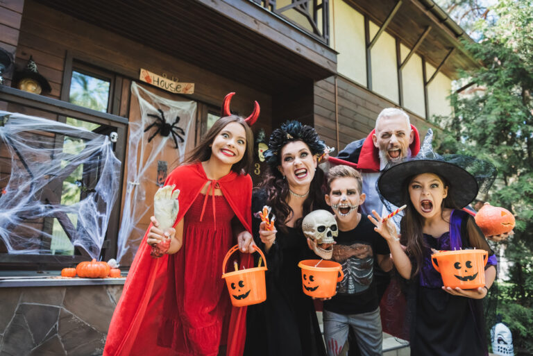 A lively Halloween gathering outside a spookily decorated house, where friends dressed in vibrant costumes share laughter and excitement. With playful props like skeletons and pumpkin buckets, they embody the festive spirit of this haunted holiday. Image Credit: lightfieldstudios/ 123rf