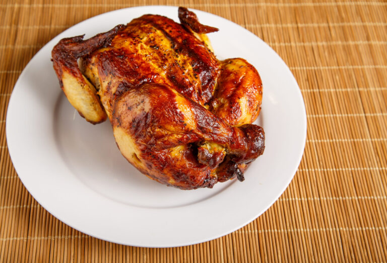 A whole roast chicken on a white plate and bamboo placemat